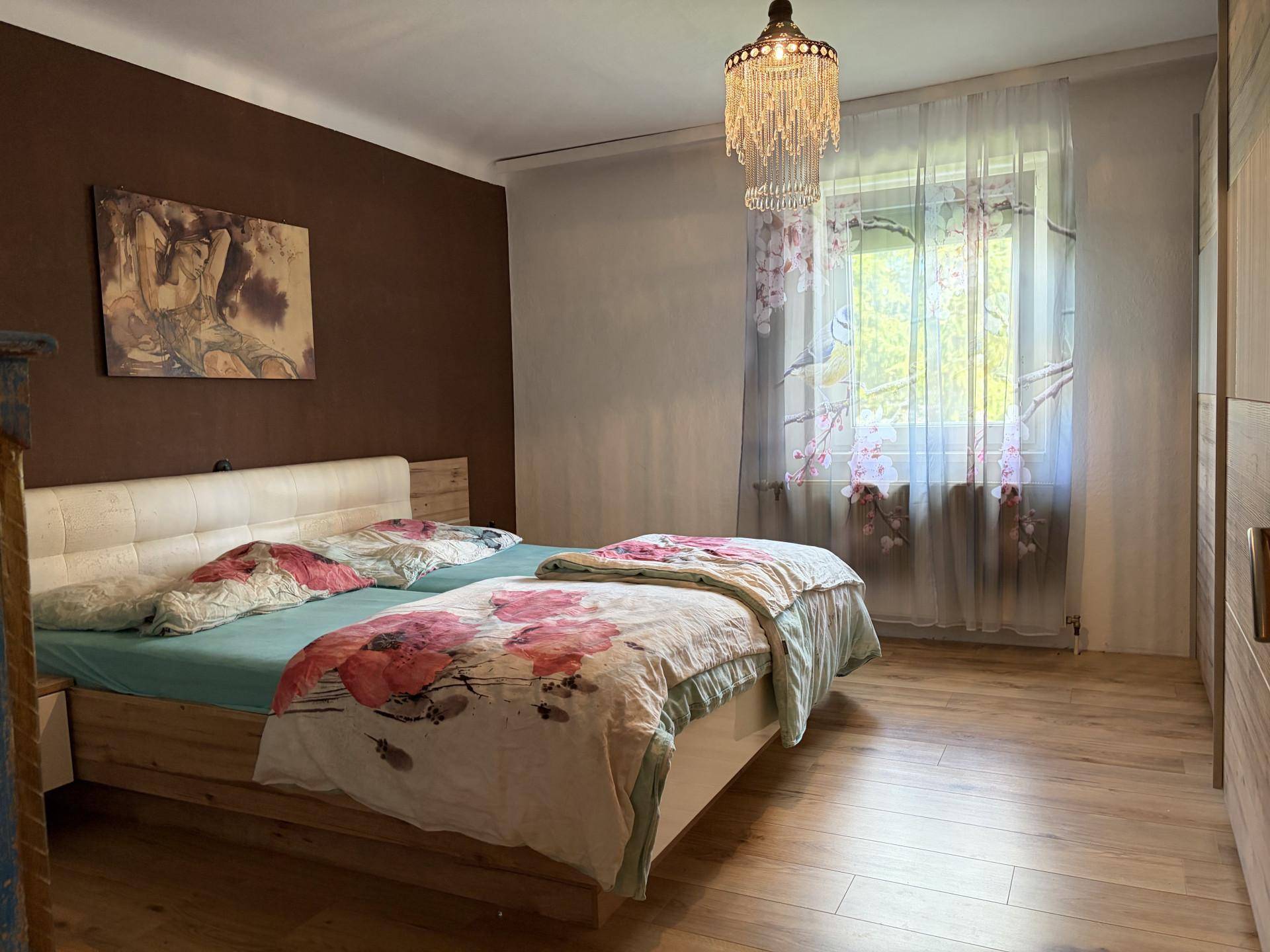 Schlafzimmer mit Holzboden, Doppelbett und großem Fenster, das viel Tageslicht hereinlässt.