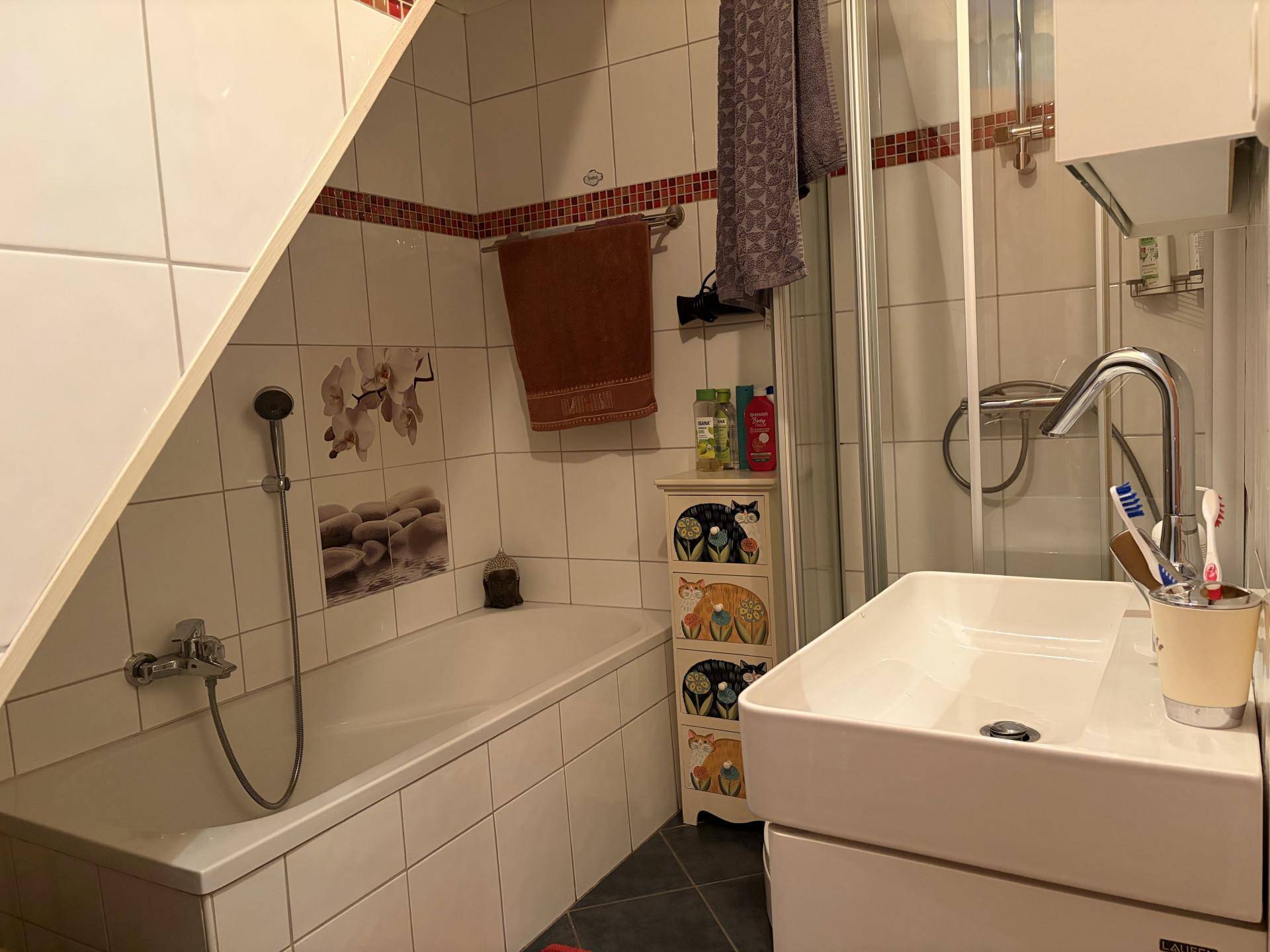 Gefliestes Badezimmer mit Badewanne, Dusche und Waschbecken unter einer Dachschräge.