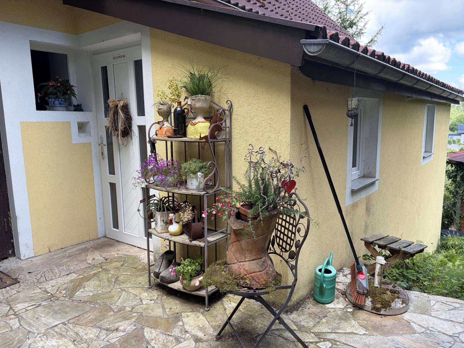 Gemütlicher Außenbereich mit Steinfliesen, dekorativen Pflanzen und einem Eingang zum Haus.