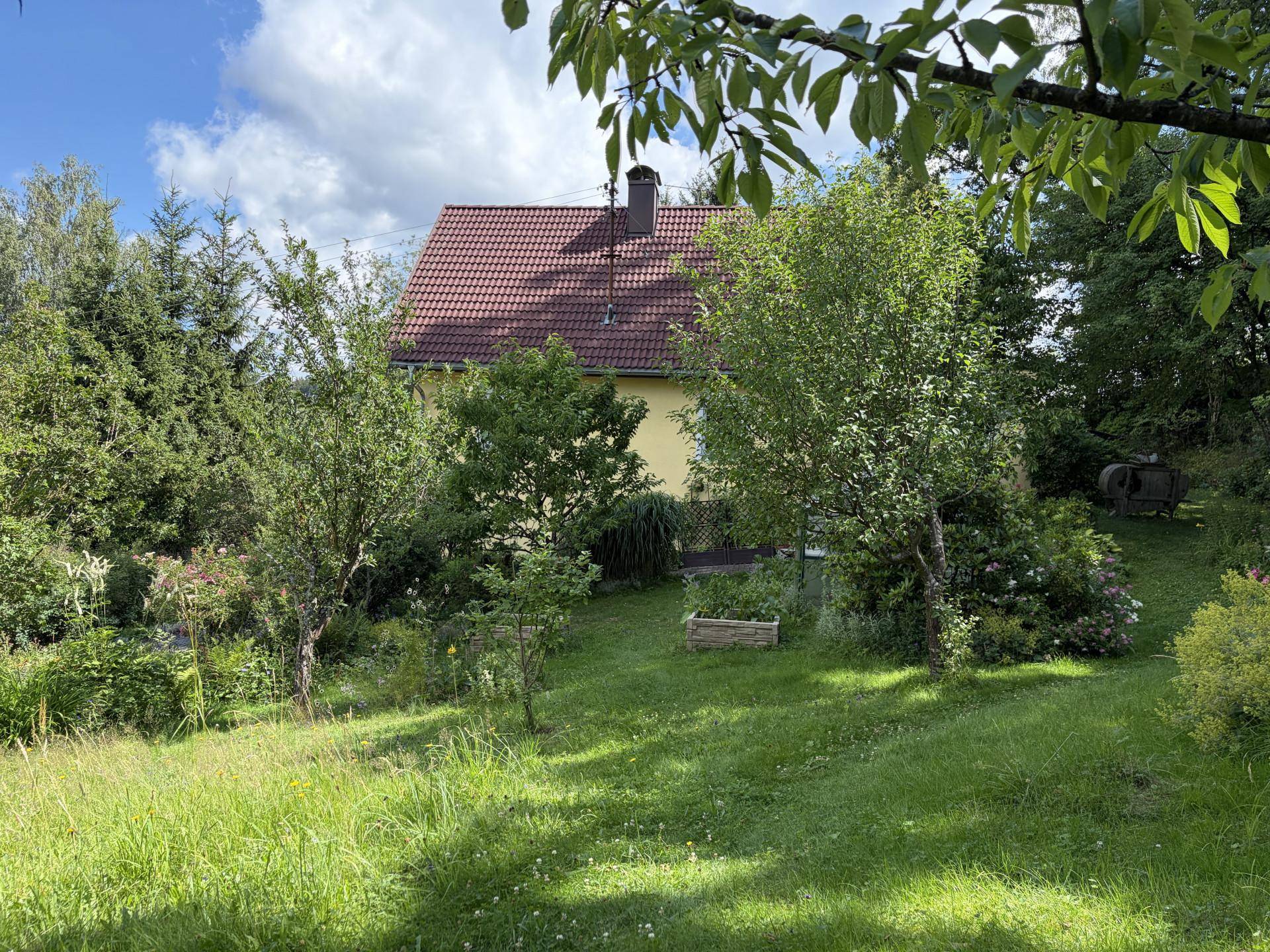 Weitläufiger Garten mit Rasen, Bäumen und einem Hochbeet, das Haus im Hintergrund.