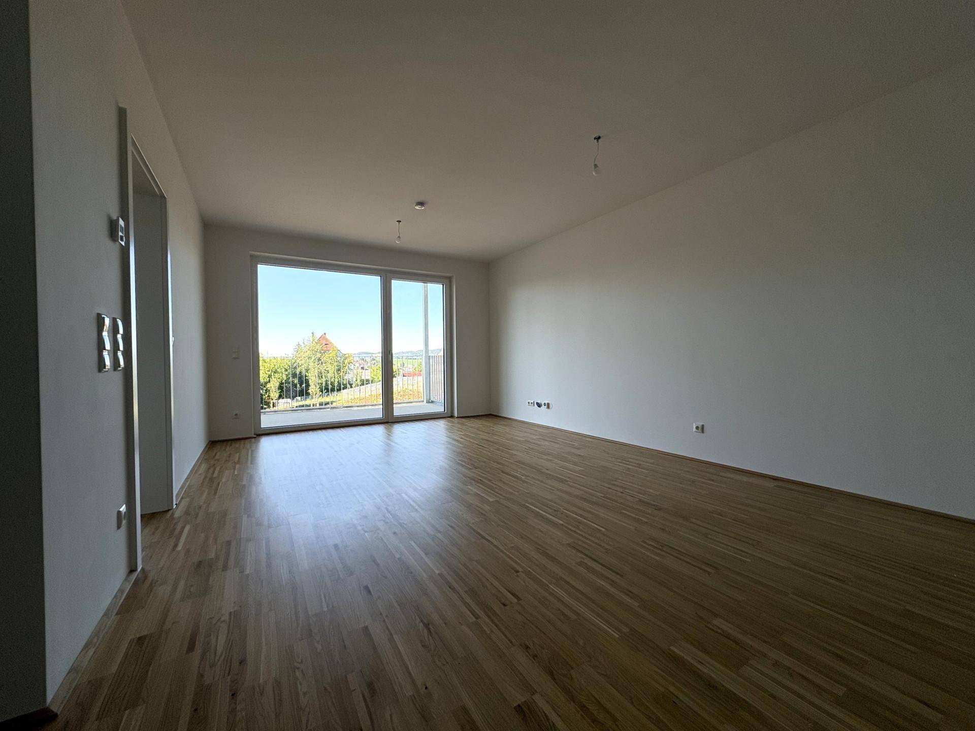 Heller Wohnbereich mit Parkettboden und großer Fensterfront, die viel Tageslicht hereinlässt.