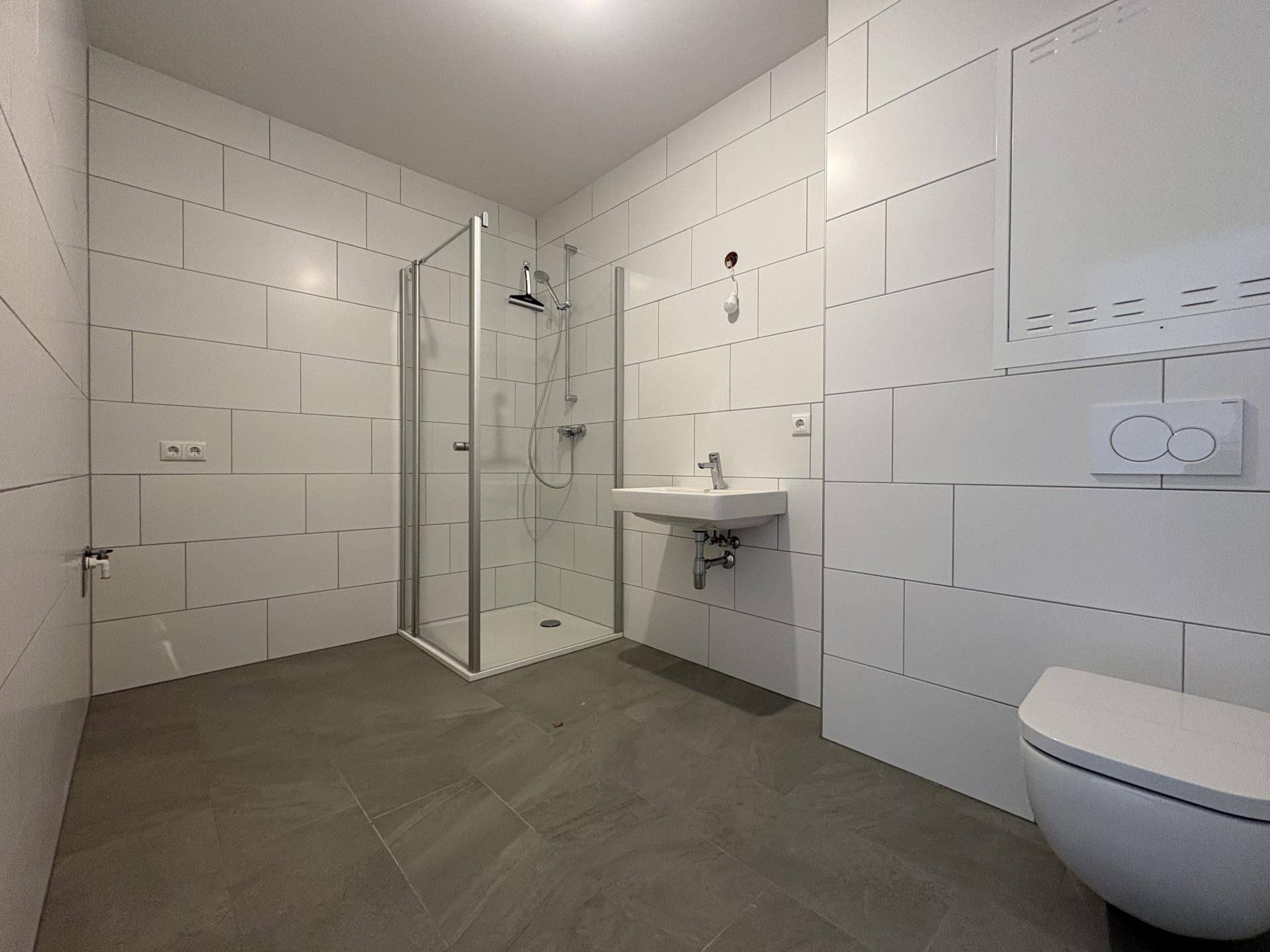 Modernes Badezimmer mit weißen Fliesen, ebenerdiger Dusche und wandhängendem WC.
