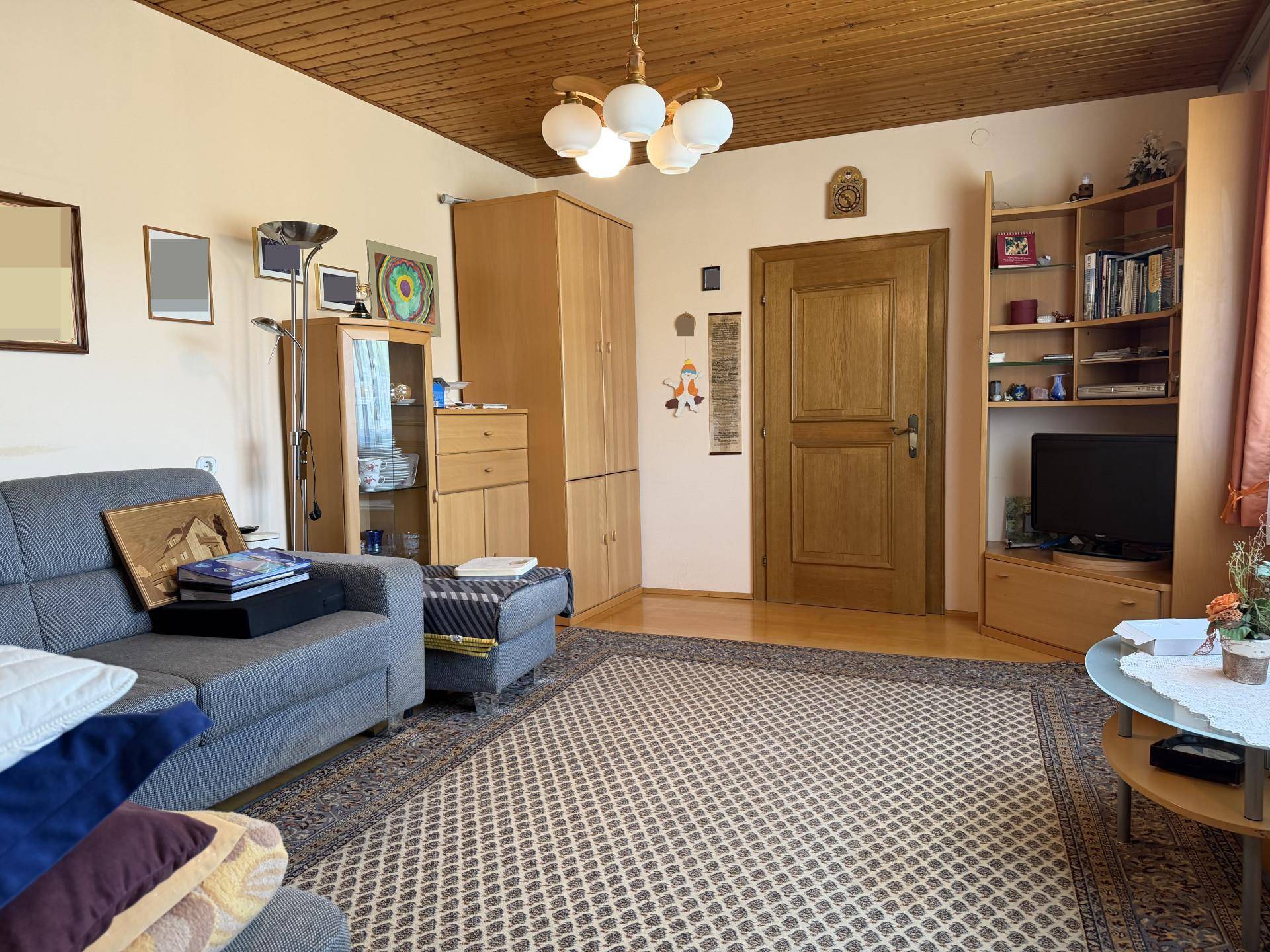 Gemütliches Wohnzimmer mit Holzbalkendecke, Teppichboden und traditionellen Möbeln.