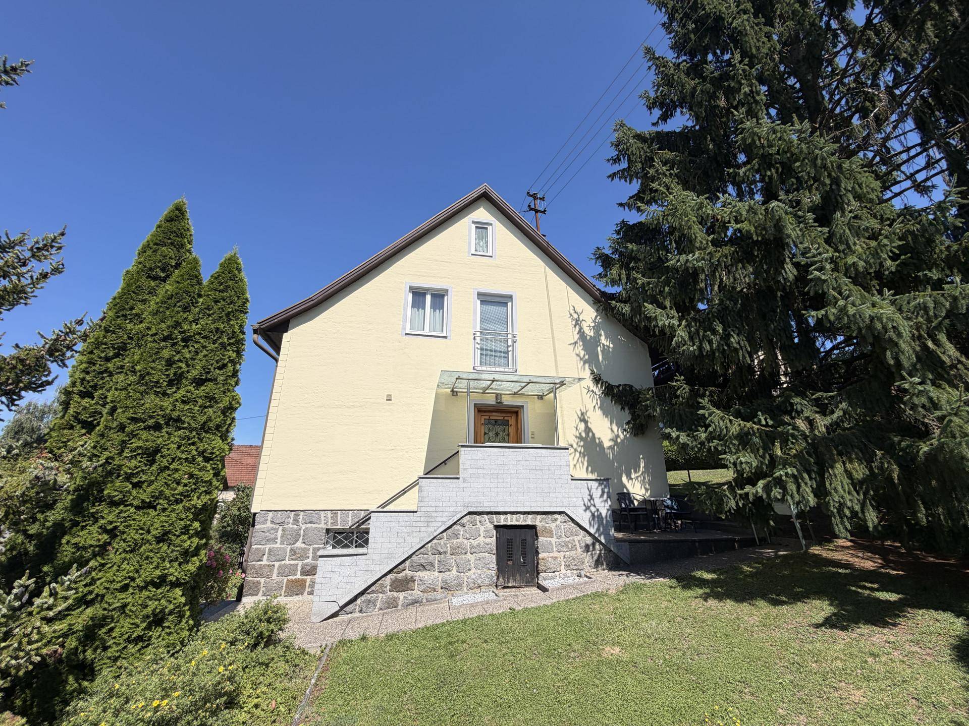 Seitenansicht des Hauses mit Außentreppe, Garten und hohen Bäumen.