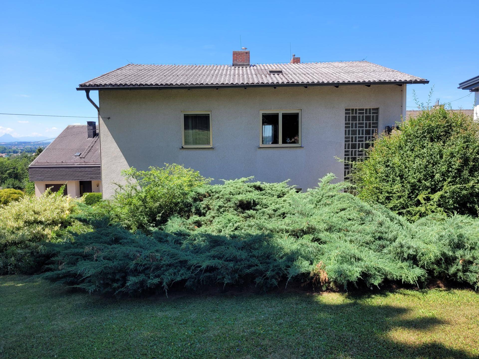 Rückansicht eines Hauses mit Satteldach, umgeben von üppigem Grün und Blick in die Ferne.