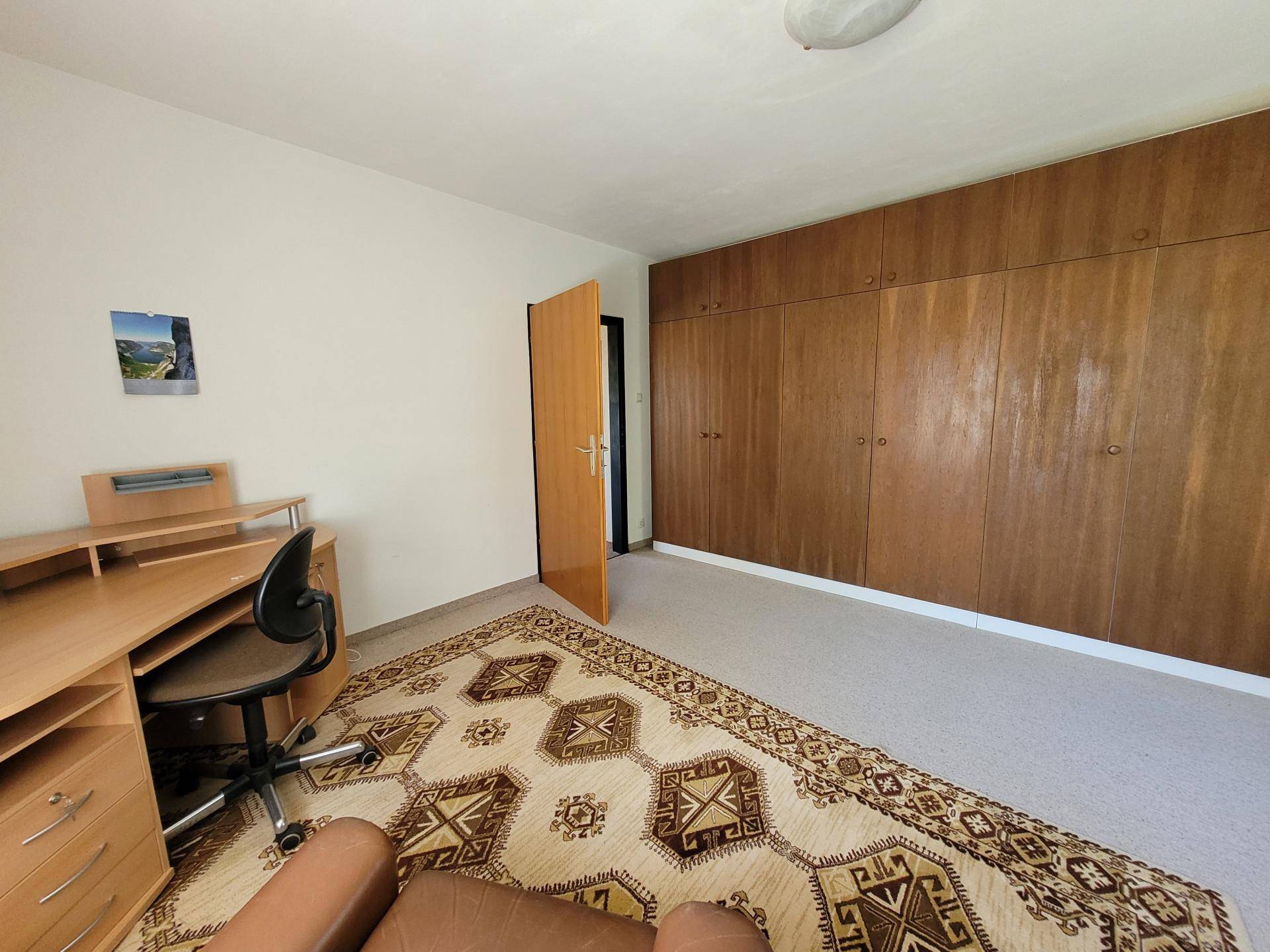 Schlafzimmer mit großen Einbauschränken aus Holz und einem Arbeitsbereich am Fenster.