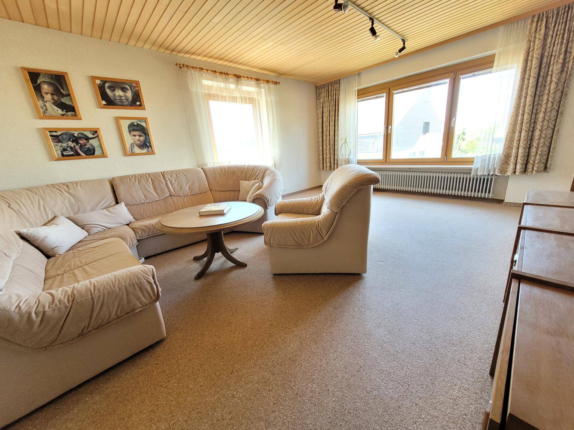 Gemütliches Wohnzimmer mit beigen Sofas, Holztäfelung an der Decke und großen Fenstern.