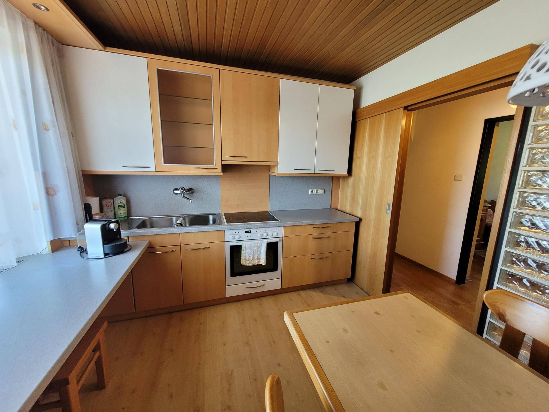 Funktionale Küche mit Holzelementen, Einbaugeräten und einem Essbereich unter Holzdecke.