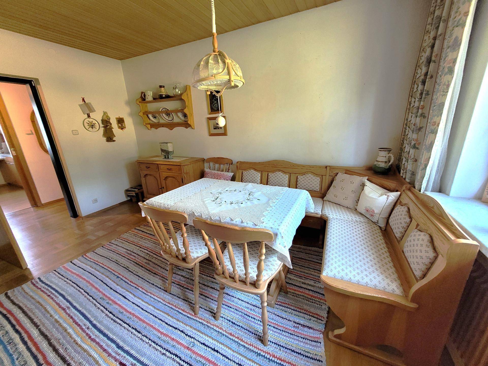 Traditioneller Essbereich mit Eckbank, Holztisch und farbenfrohem Teppich unter Holzdecke.
