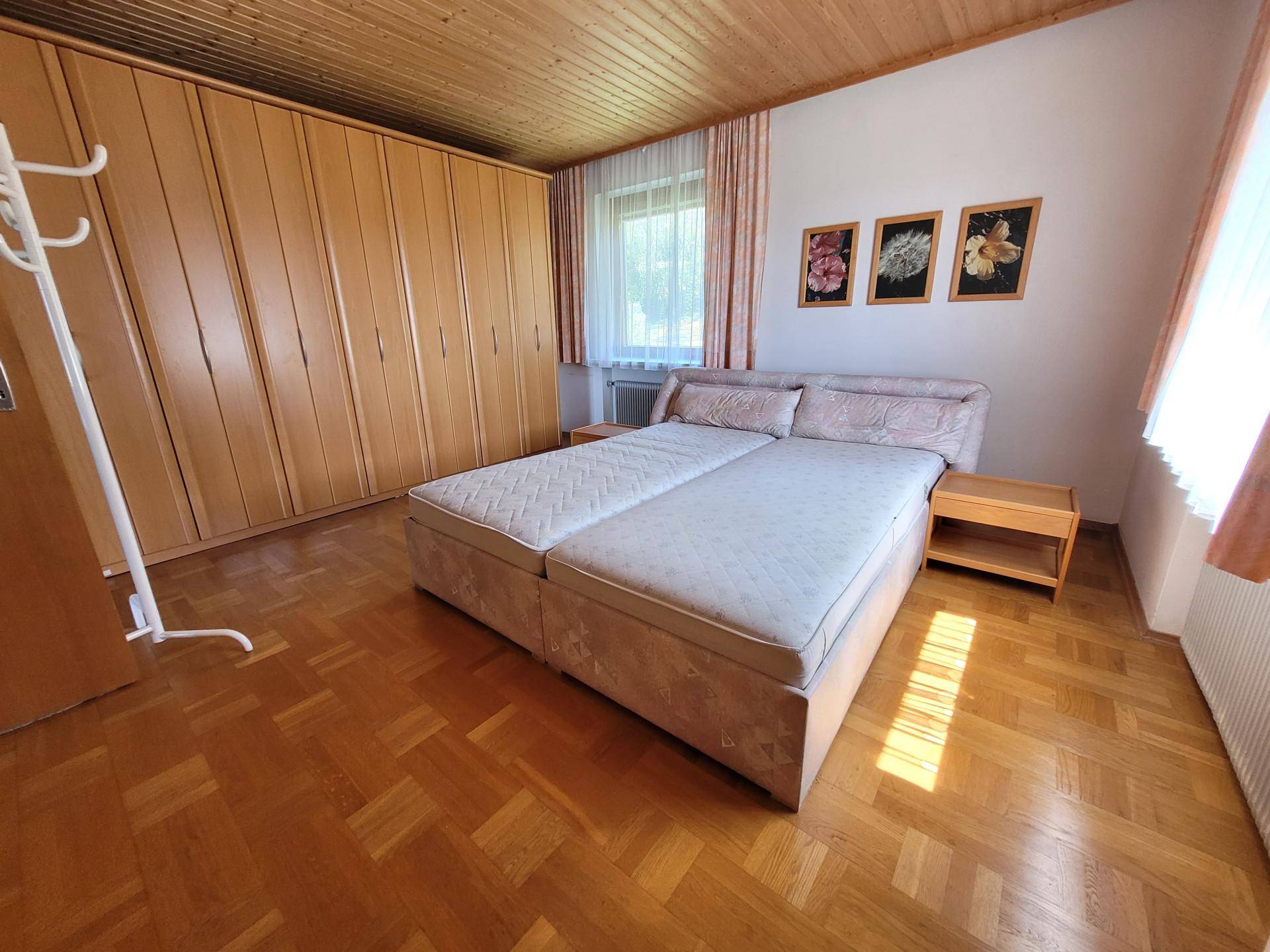 Helles Schlafzimmer mit Doppelbett, Holzschrankwand und Parkettboden unter Holzdecke.