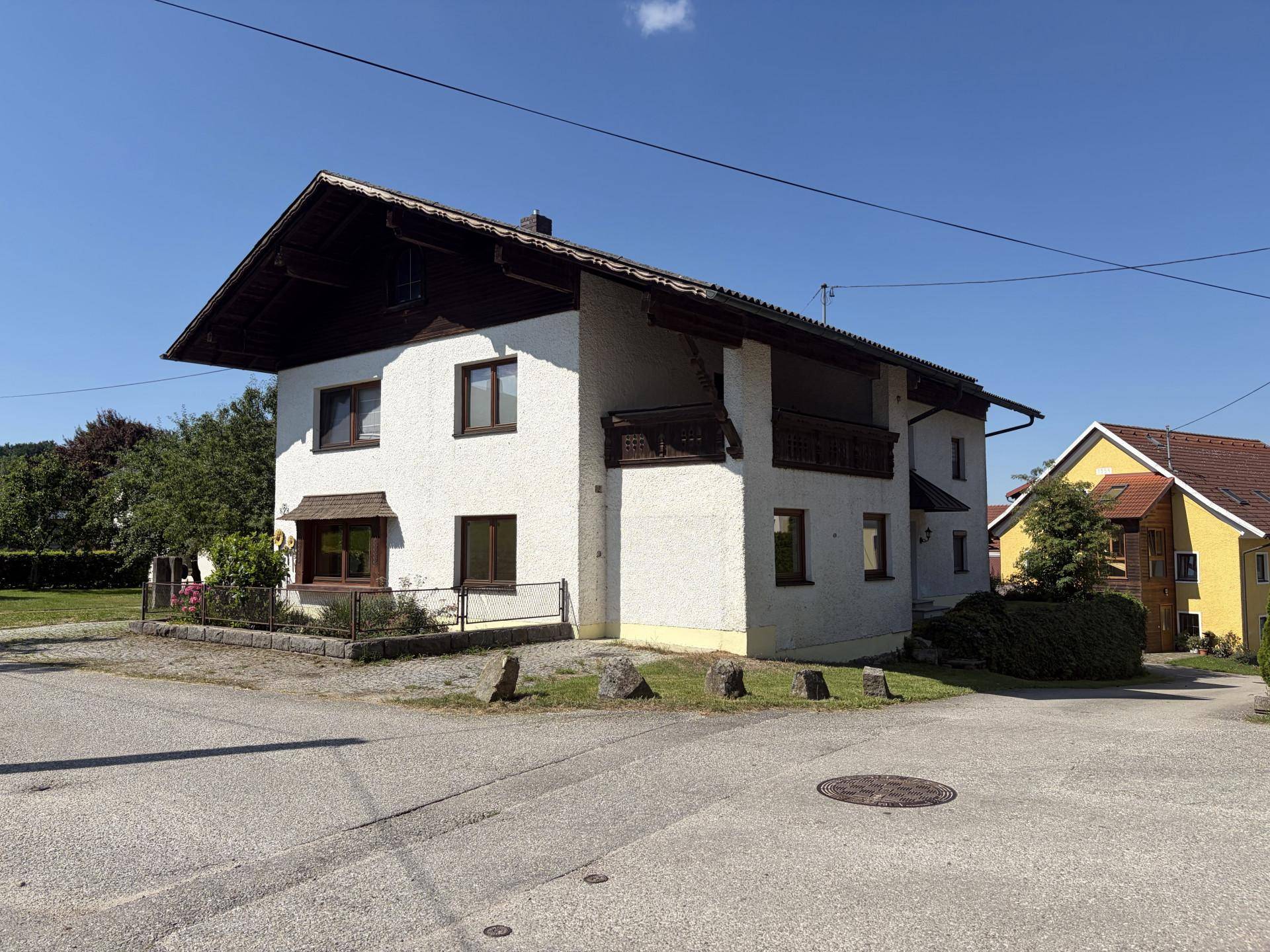 Ansicht des Einfamilienhauses von einer anderen Seite mit Balkon und gepflegter Umgebung unter blauem Himmel.