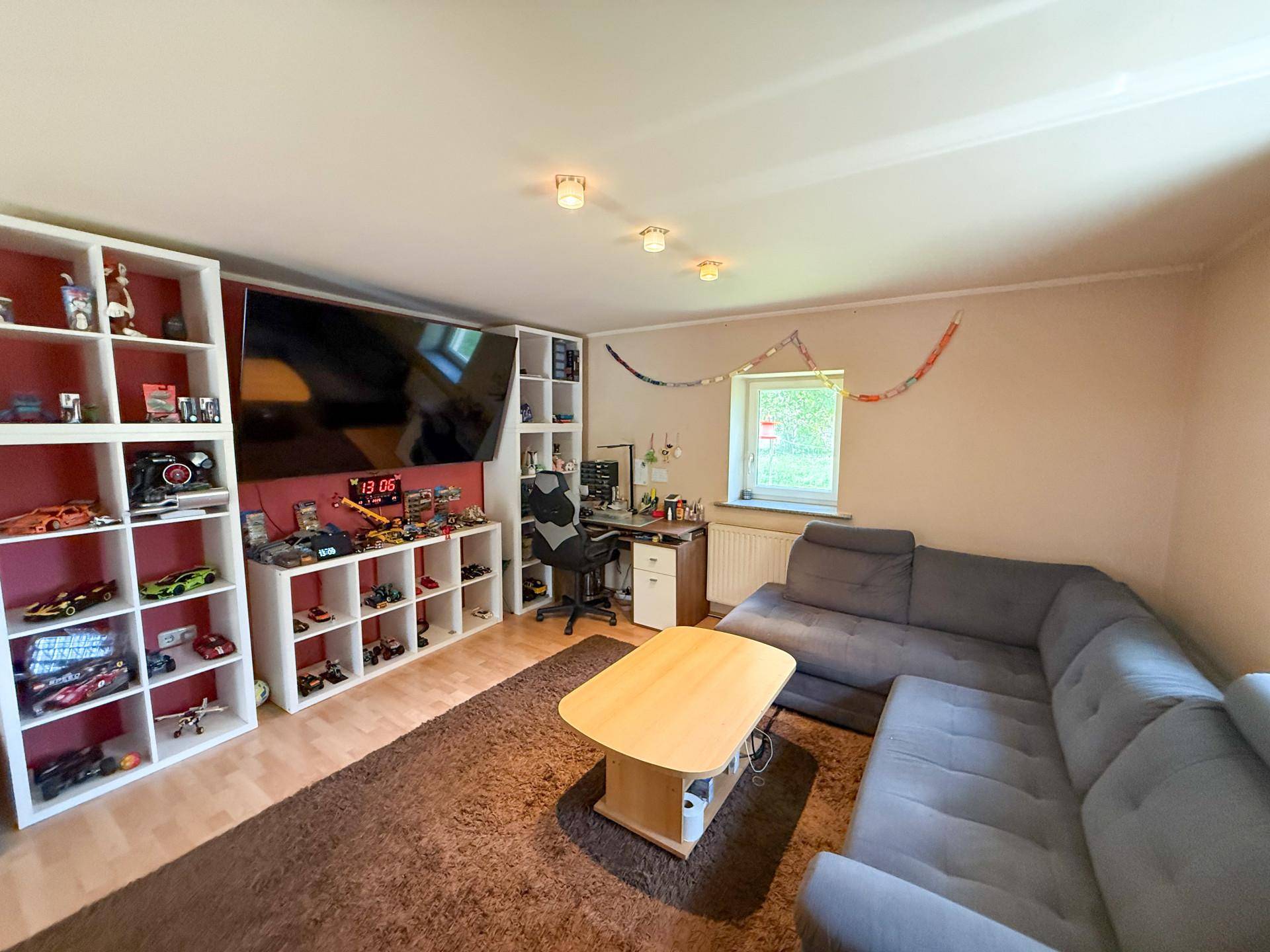 Gemütliches Wohnzimmer mit großem Ecksofa, Fernseher und Regalen für Spielzeug, hell und einladend.