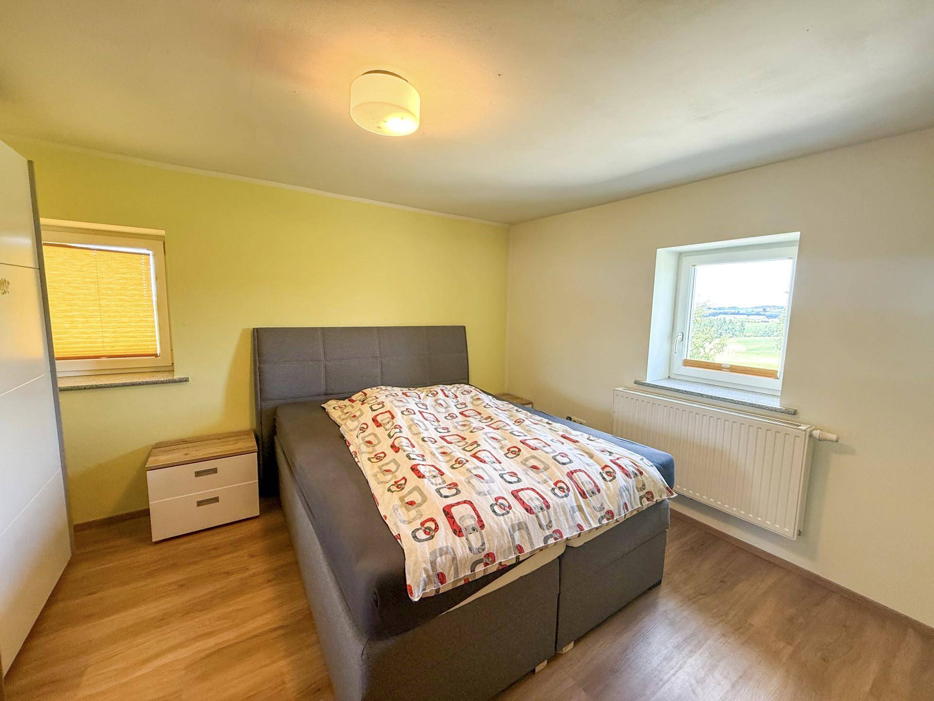 Helles Schlafzimmer mit Doppelbett, Nachttischen und einem Fenster mit Blick ins Grüne, einladend gestaltet.