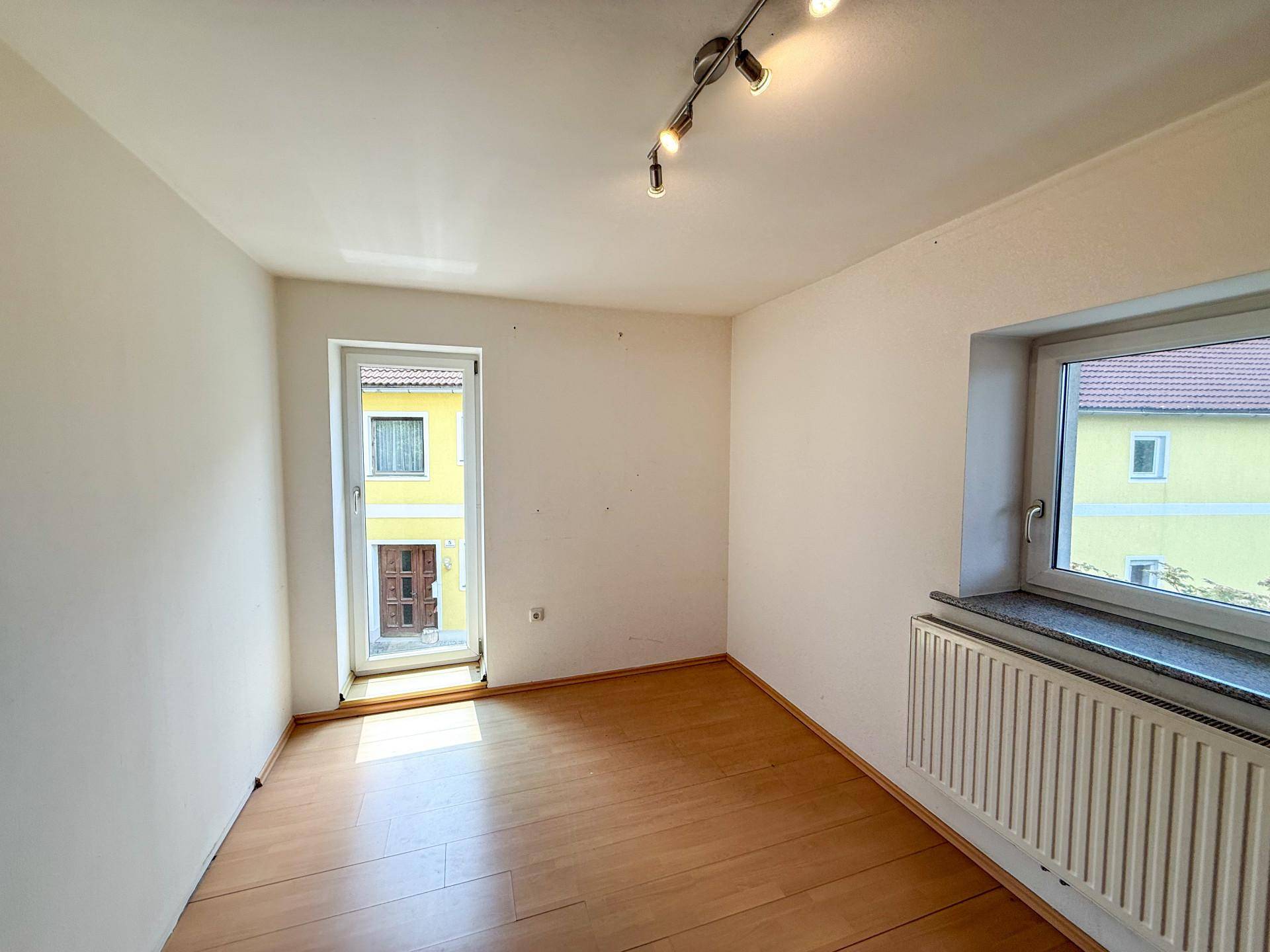 Leeres Zimmer mit Laminatboden und Fenster, das einen Blick auf das Nachbargebäude bietet, vielseitig nutzbar.