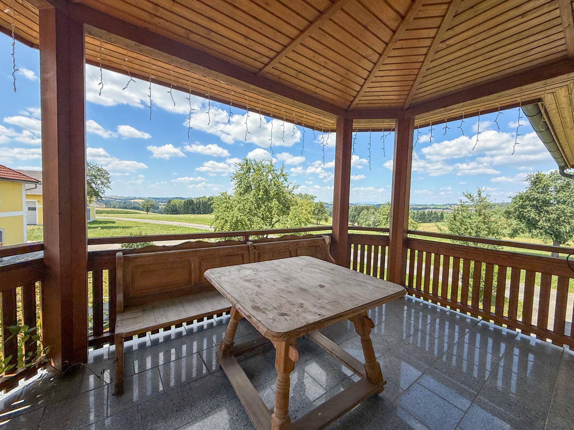 Überdachter Holzbalkon mit Sitzgelegenheiten und weitem Blick über die grüne Landschaft, ideal zum Entspannen.