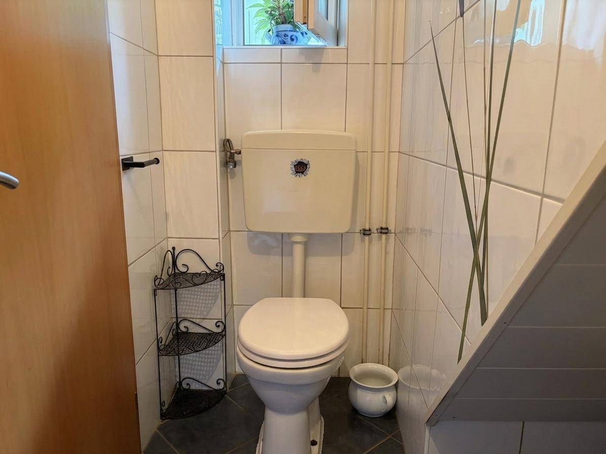 Kleines WC mit Fenster, gefliesten Wänden und einem Stand-WC unter der Dachschräge.