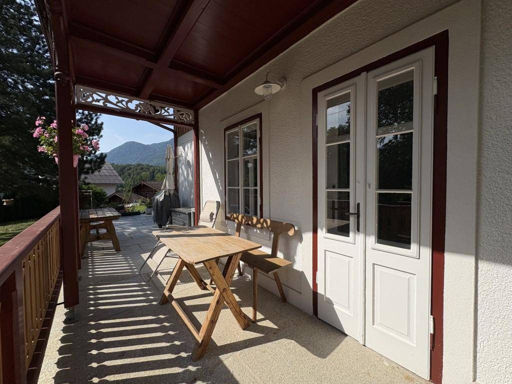 Gemütliche überdachte Terrasse mit Holztisch und Stühlen, ideal für Mahlzeiten im Freien mit Bergblick.