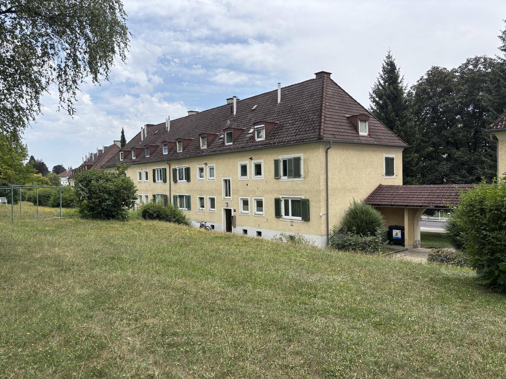 Ansicht des gelben Wohnhauses mit grünen Fensterläden und weitläufiger Rasenfläche im Vordergrund.
