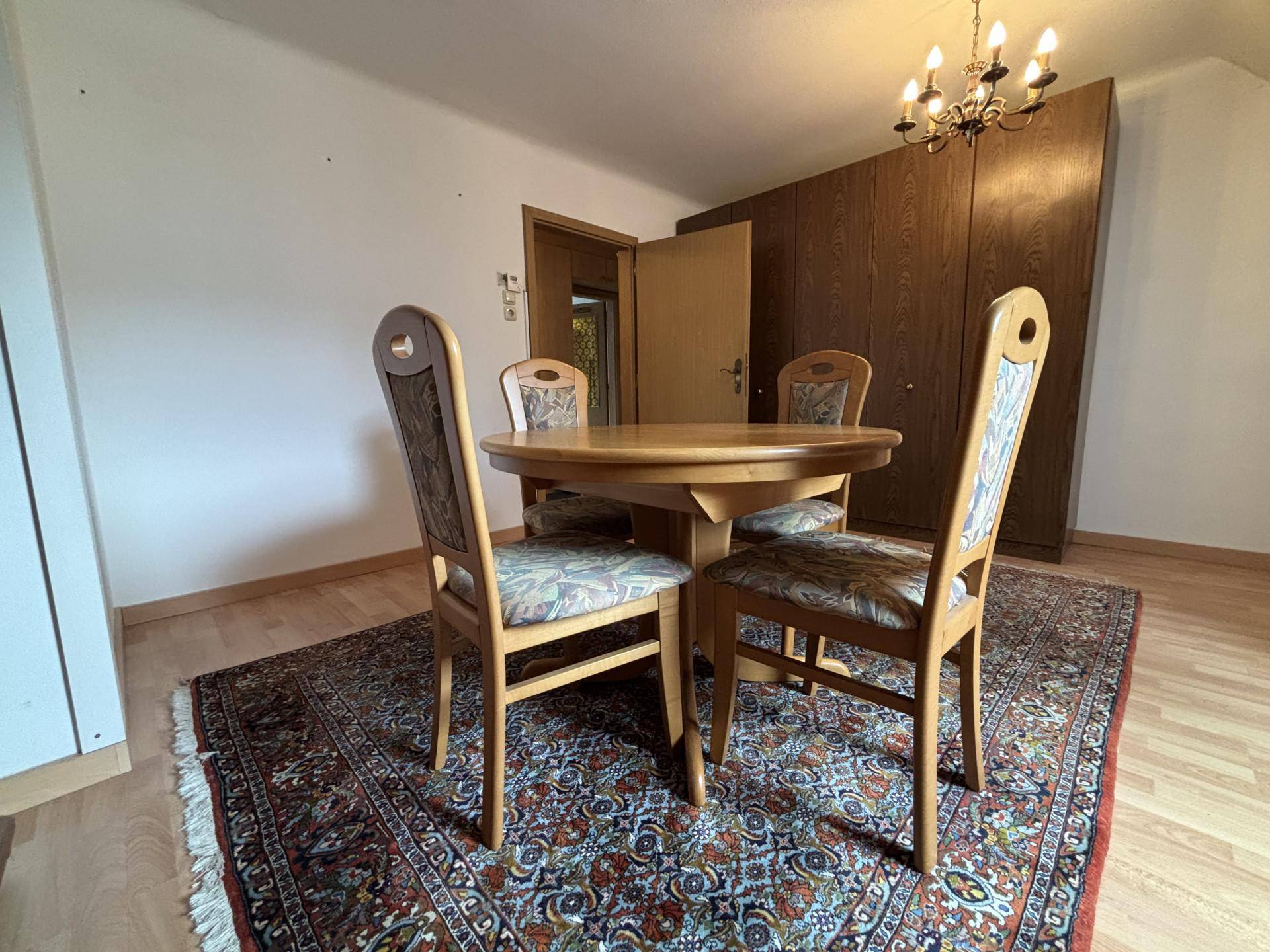 Essbereich mit Holztisch und Stühlen, einem gemusterten Teppich und einem großen Holzschrank.