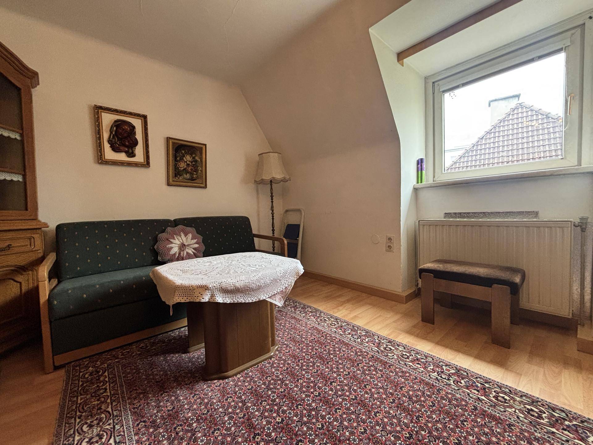 Gemütliches Wohnzimmer mit grünem Sofa, kleinem Tisch und Fenster mit Blick auf ein Ziegeldach.