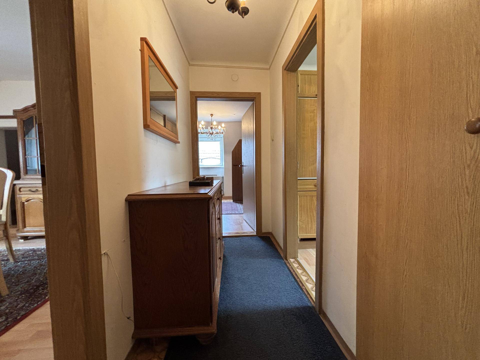 Flur mit dunklem Teppich, Holzkommode und Zugang zu verschiedenen Zimmern der Wohnung.