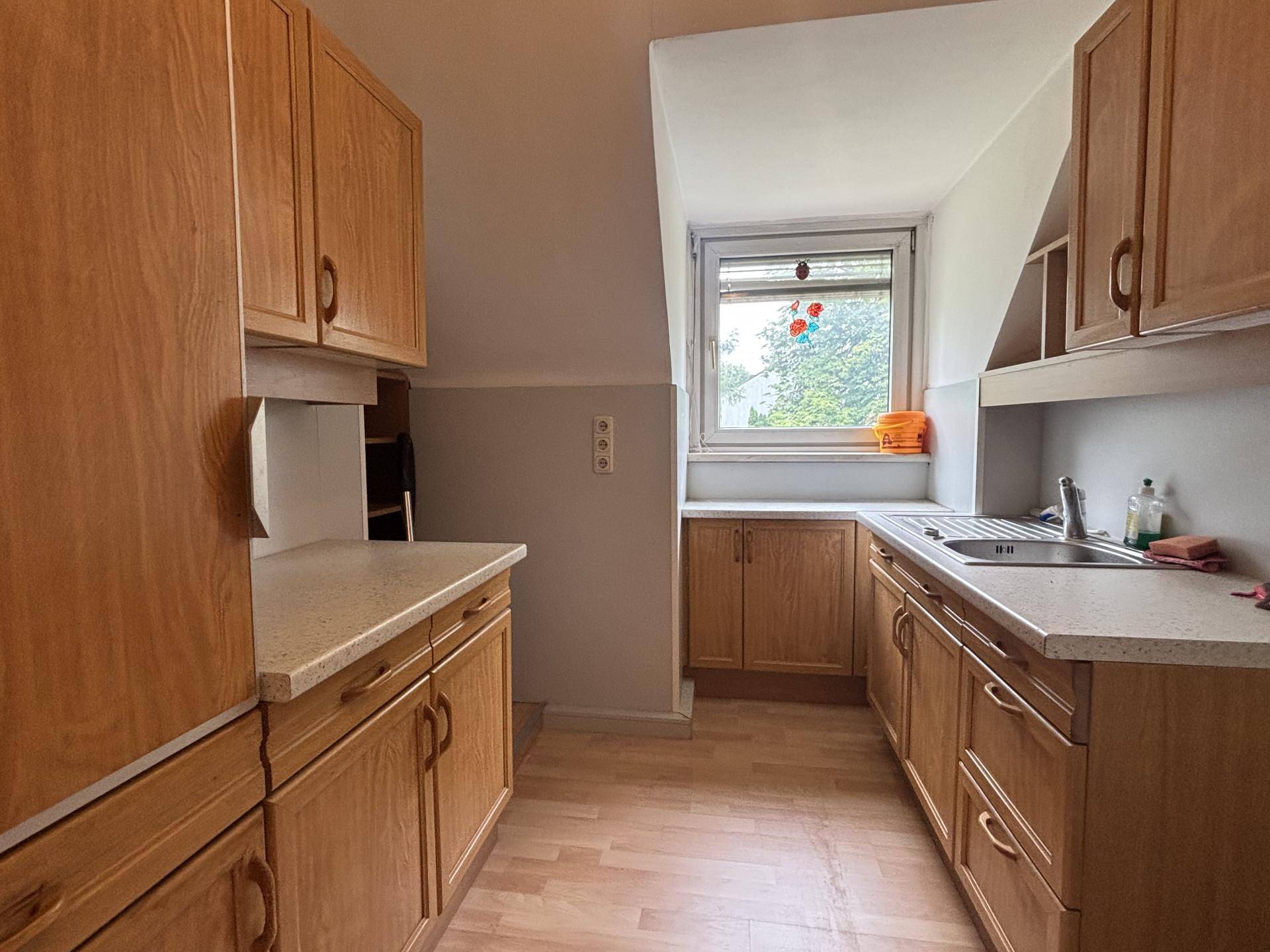 Helle Küche mit Holzfronten, Arbeitsplatte und Fenster, das Tageslicht hereinlässt.