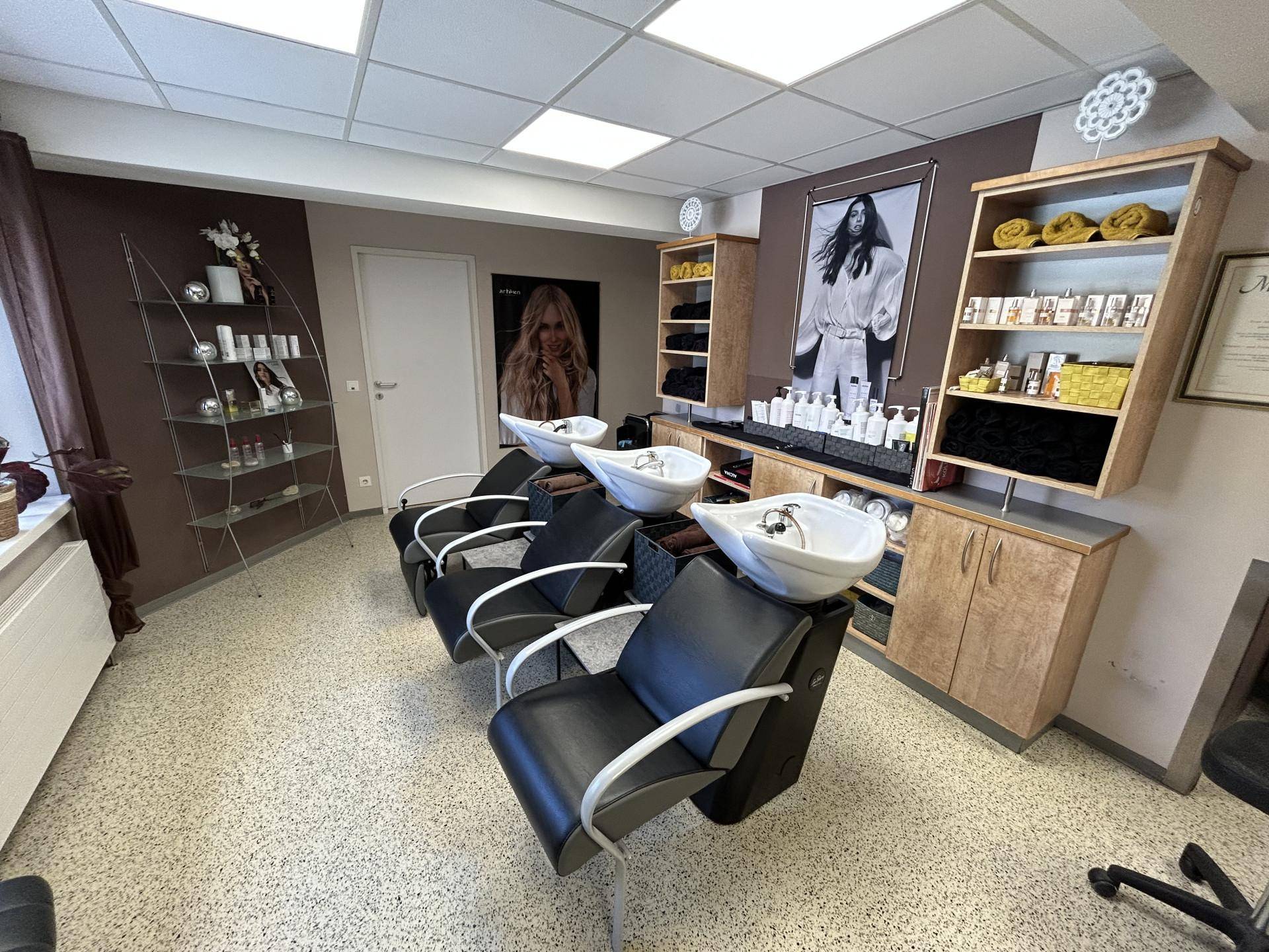 Detailansicht des Haarwaschbereichs im Friseursalon mit drei Stühlen und Regalen für Produkte.