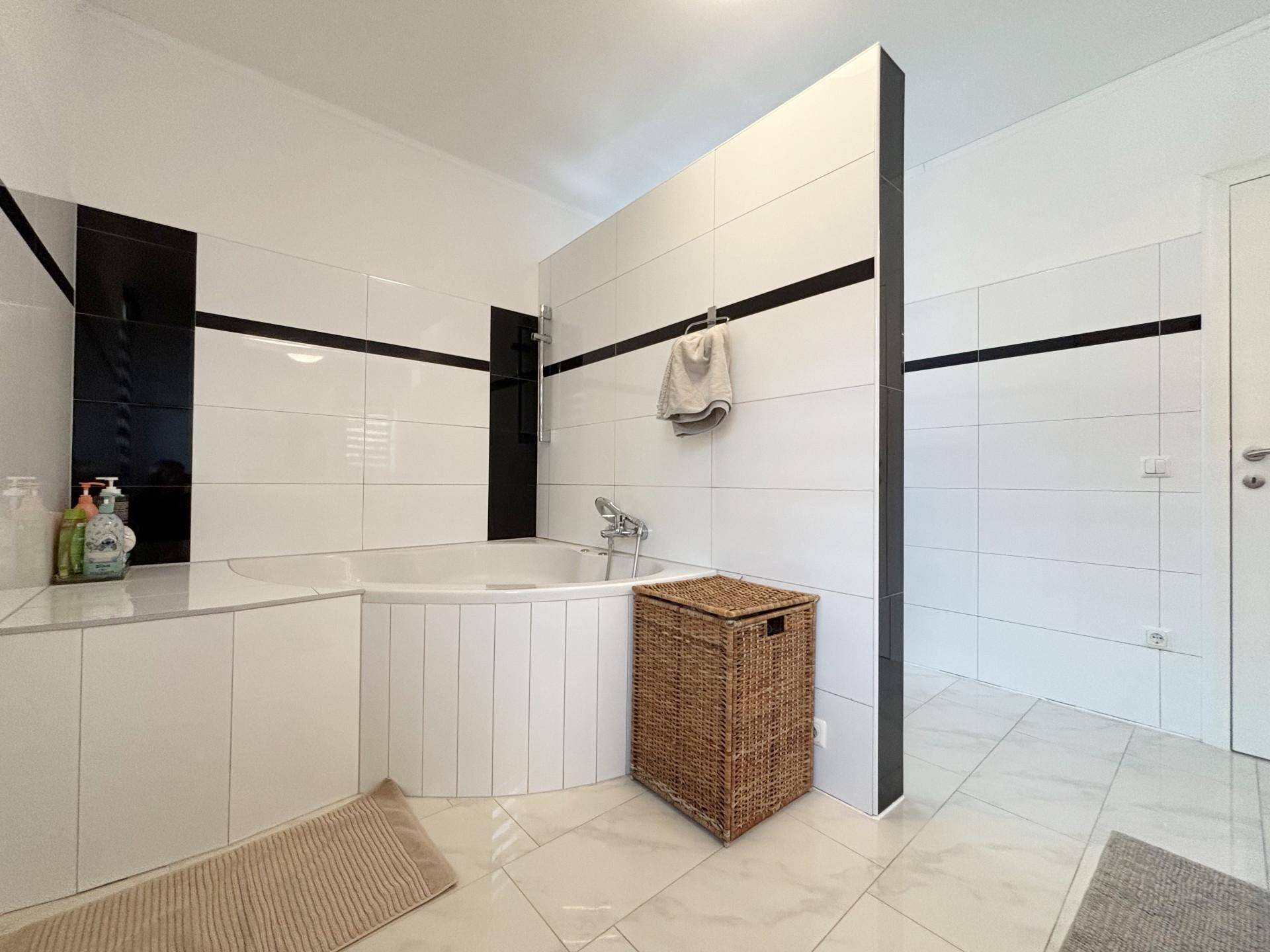 Geräumiges Badezimmer mit Eckbadewanne und weißen Fliesen mit schwarzem Dekorstreifen.