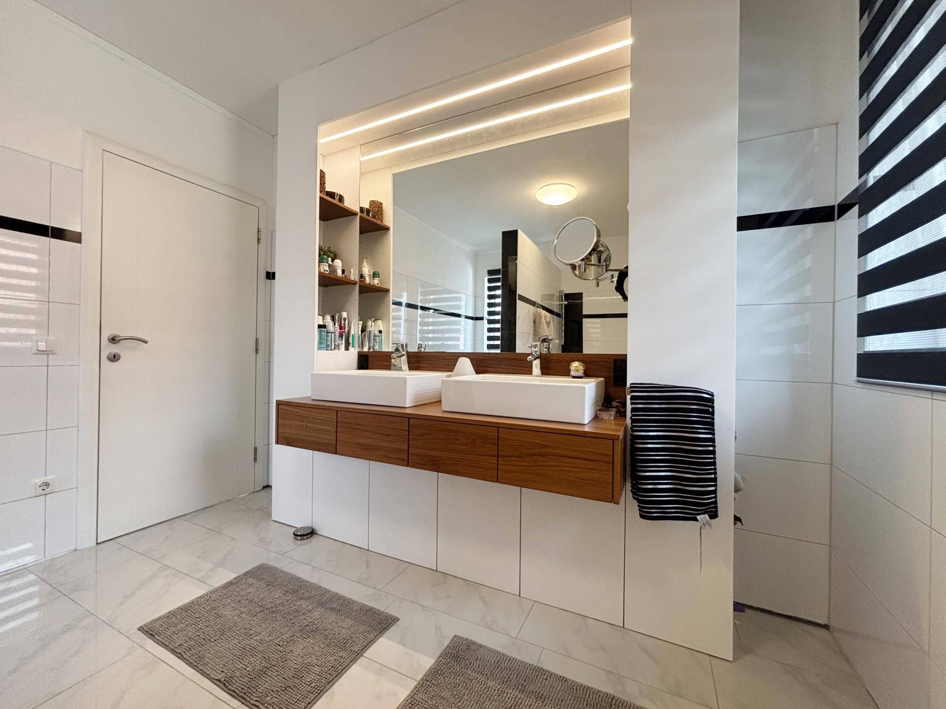 Großes Badezimmer mit Doppelwaschbecken, beleuchtetem Spiegel und modernen Holzmöbeln.