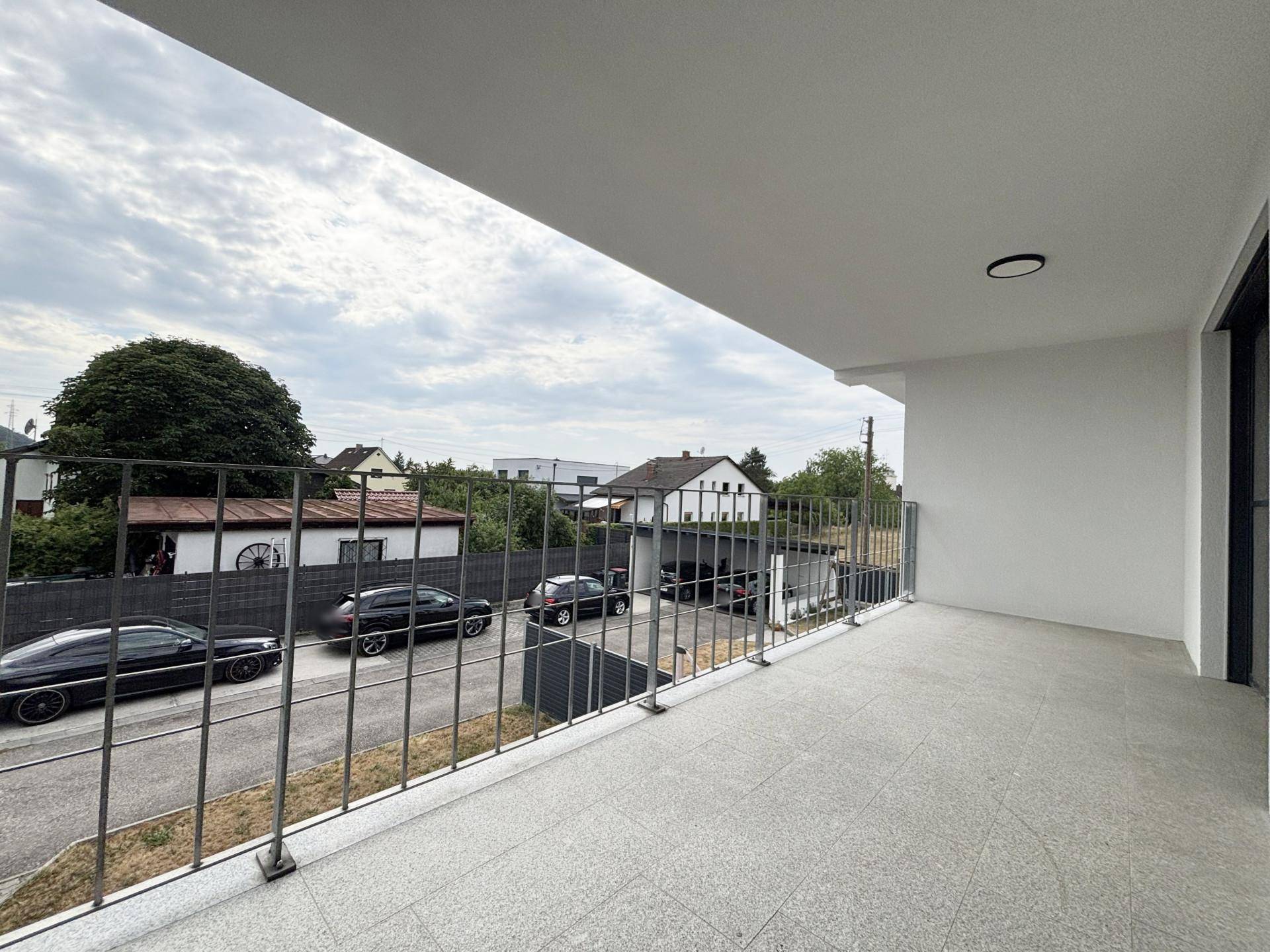 Geräumiger Balkon mit Metallgeländer und Blick auf die Umgebung und Nachbarhäuser.