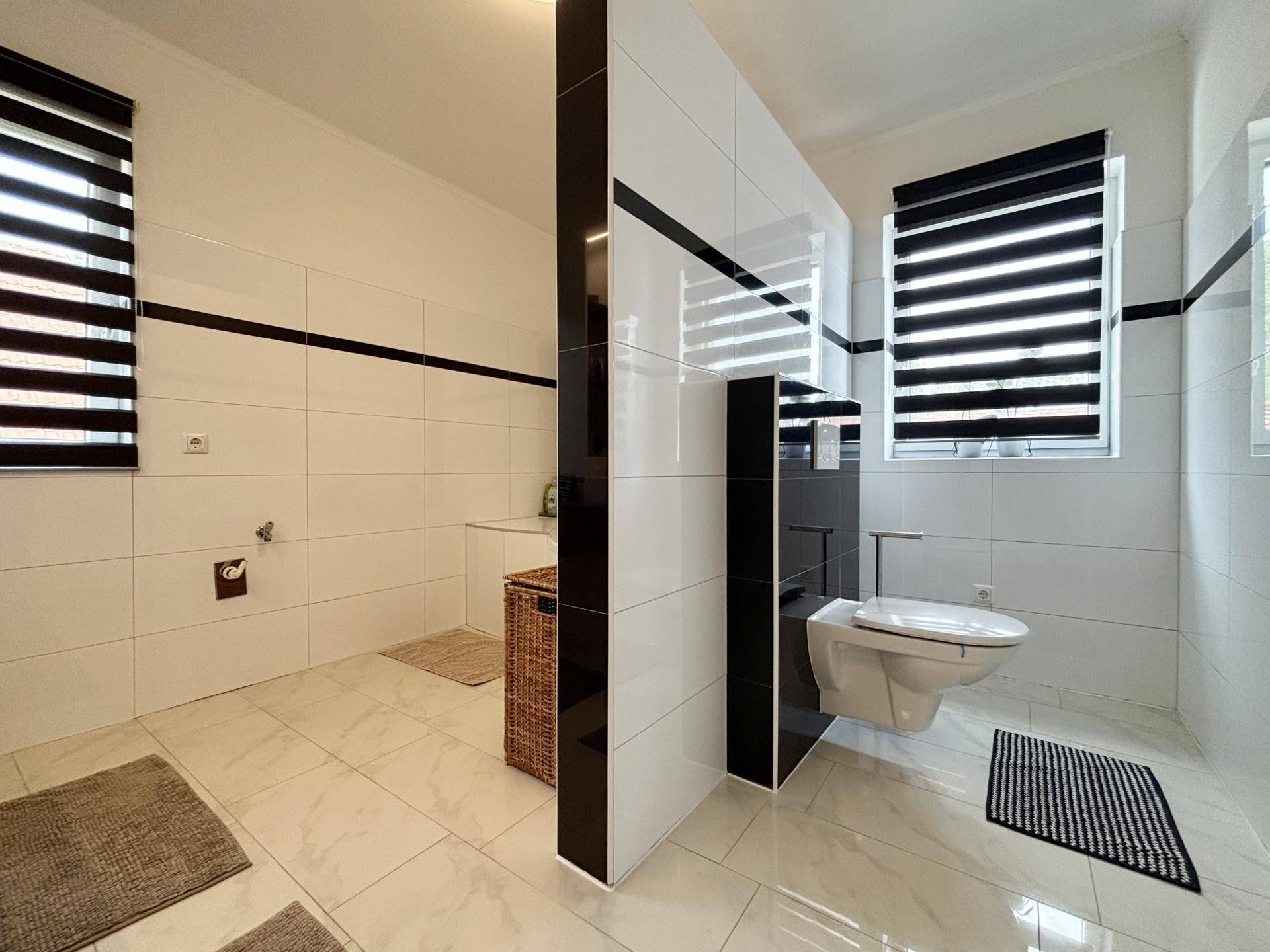 Helles Badezimmer mit wandhängendem WC, Fenster und modernen Fliesen in Weiß und Schwarz.