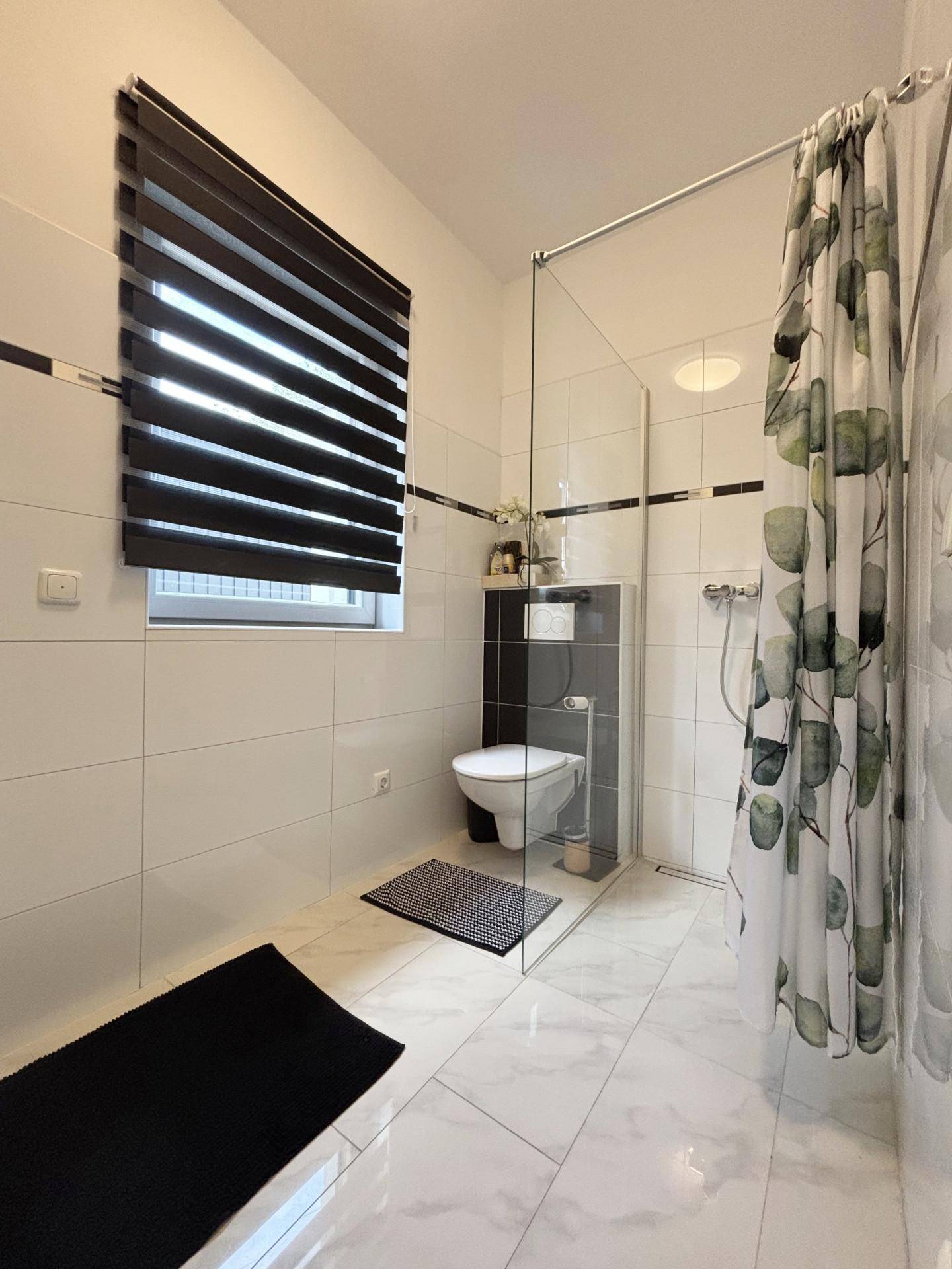 Modernes Badezimmer mit Dusche, wandhängendem WC und weißen Fliesen mit schwarzem Akzent.