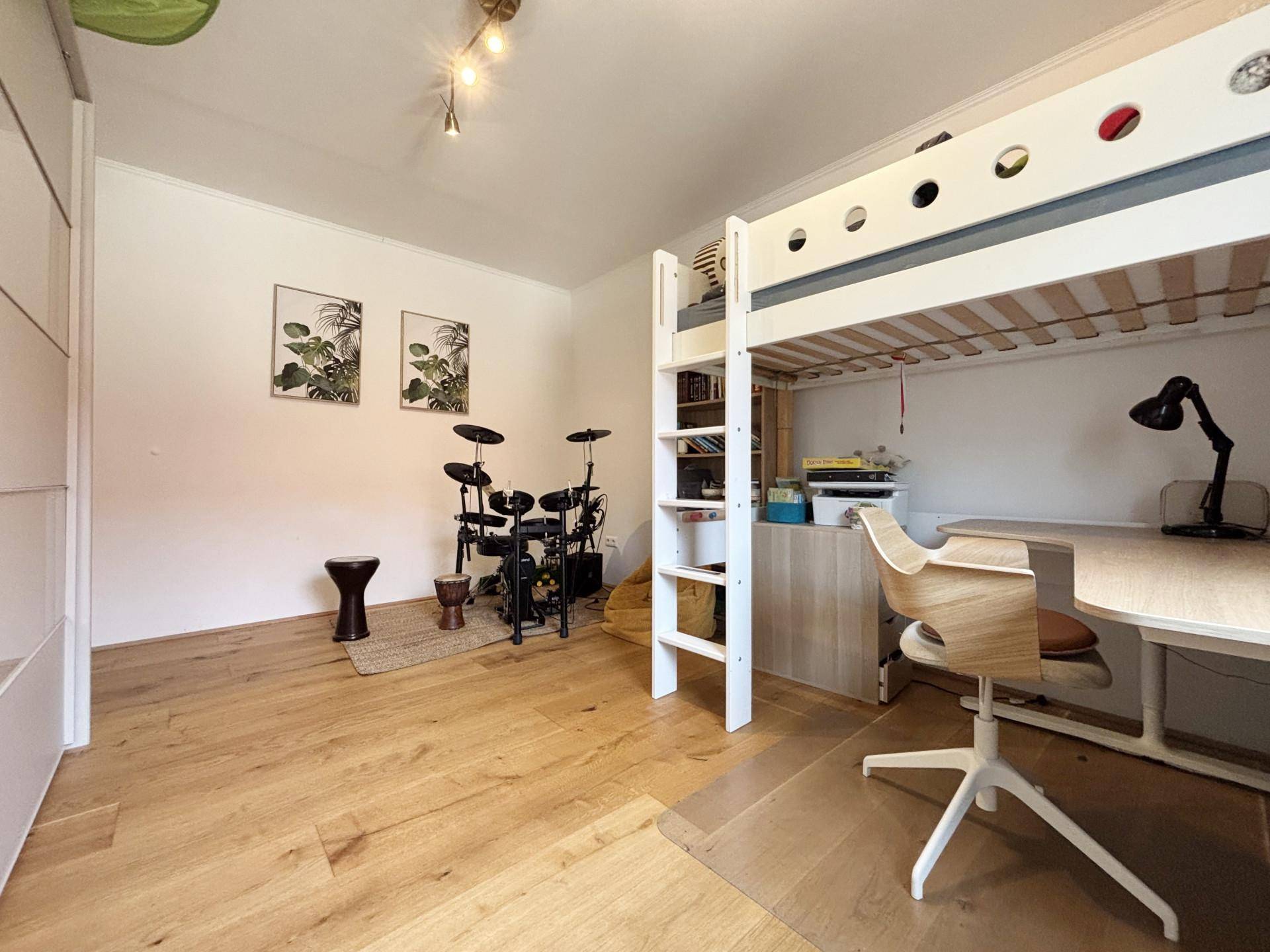 Kinderzimmer mit Hochbett, Schreibtisch, Schlagzeug und hellem Holzfußboden.