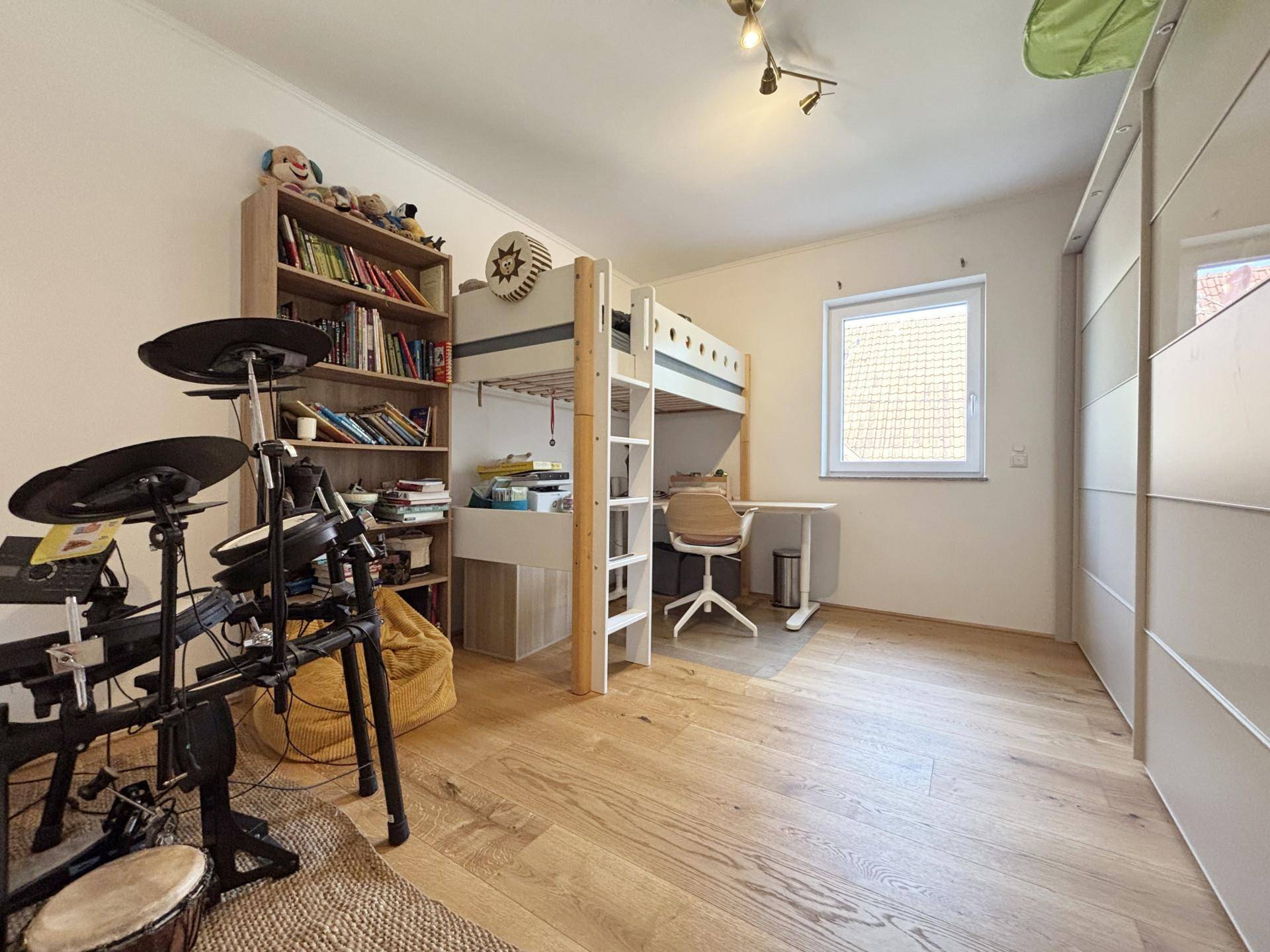 Helles Kinderzimmer mit Hochbett, Schreibtisch, Bücherregal und großem Kleiderschrank.