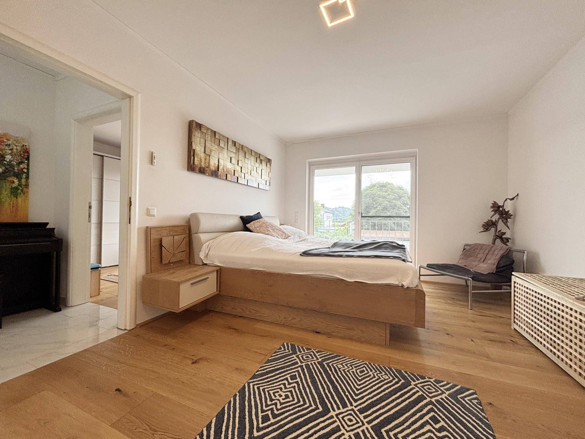 Helles Schlafzimmer mit modernem Holzbett, Holzboden und Zugang zum Balkon.