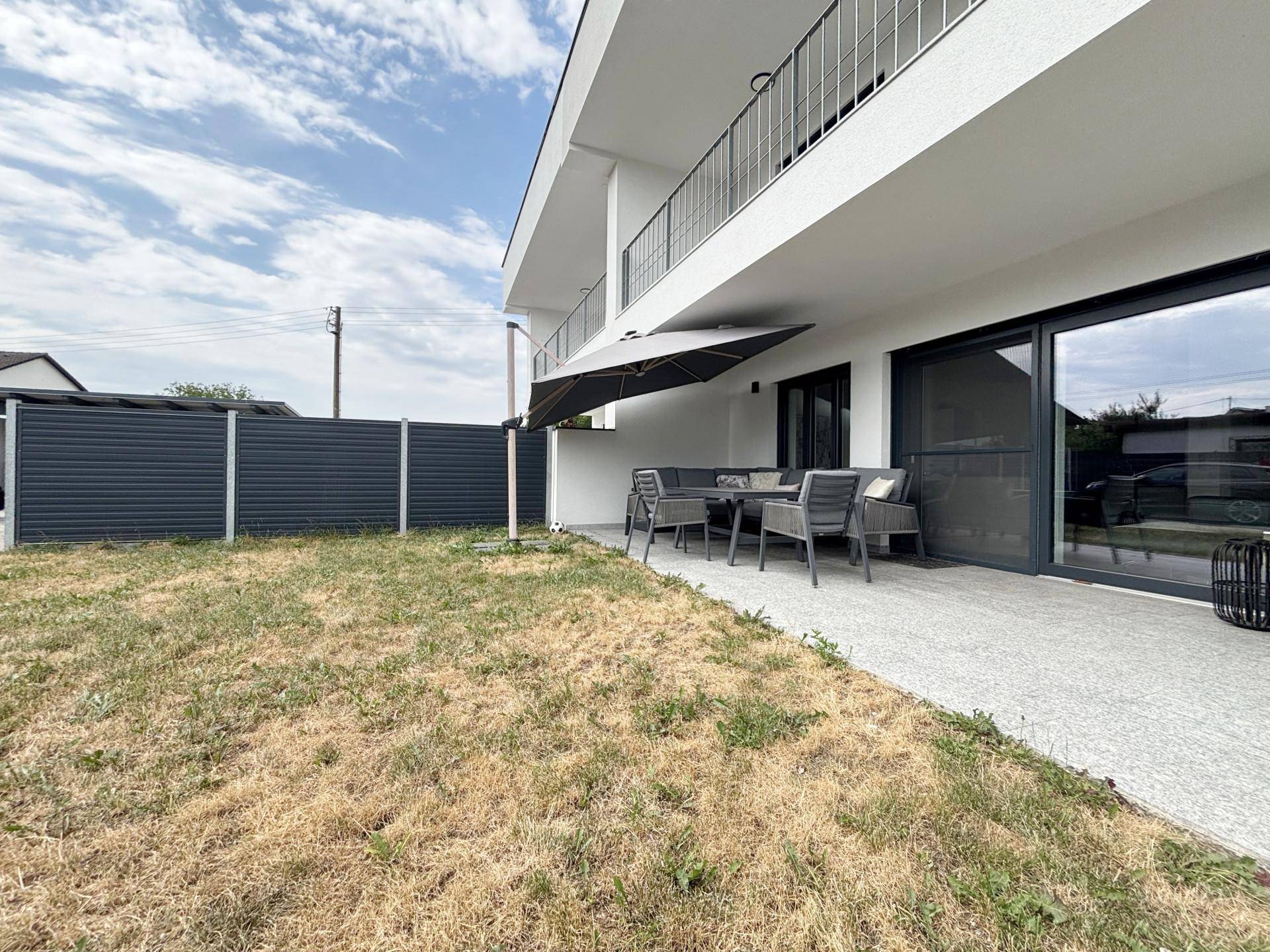Gemütliche Terrasse mit Gartenmöbeln und Sonnenschirm neben einem kleinen Rasenbereich.