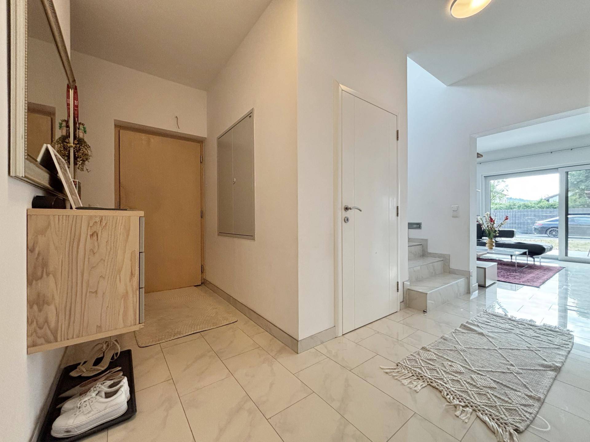 Heller Eingangsbereich mit Fliesenboden, Garderobe und Blick ins Wohnzimmer.