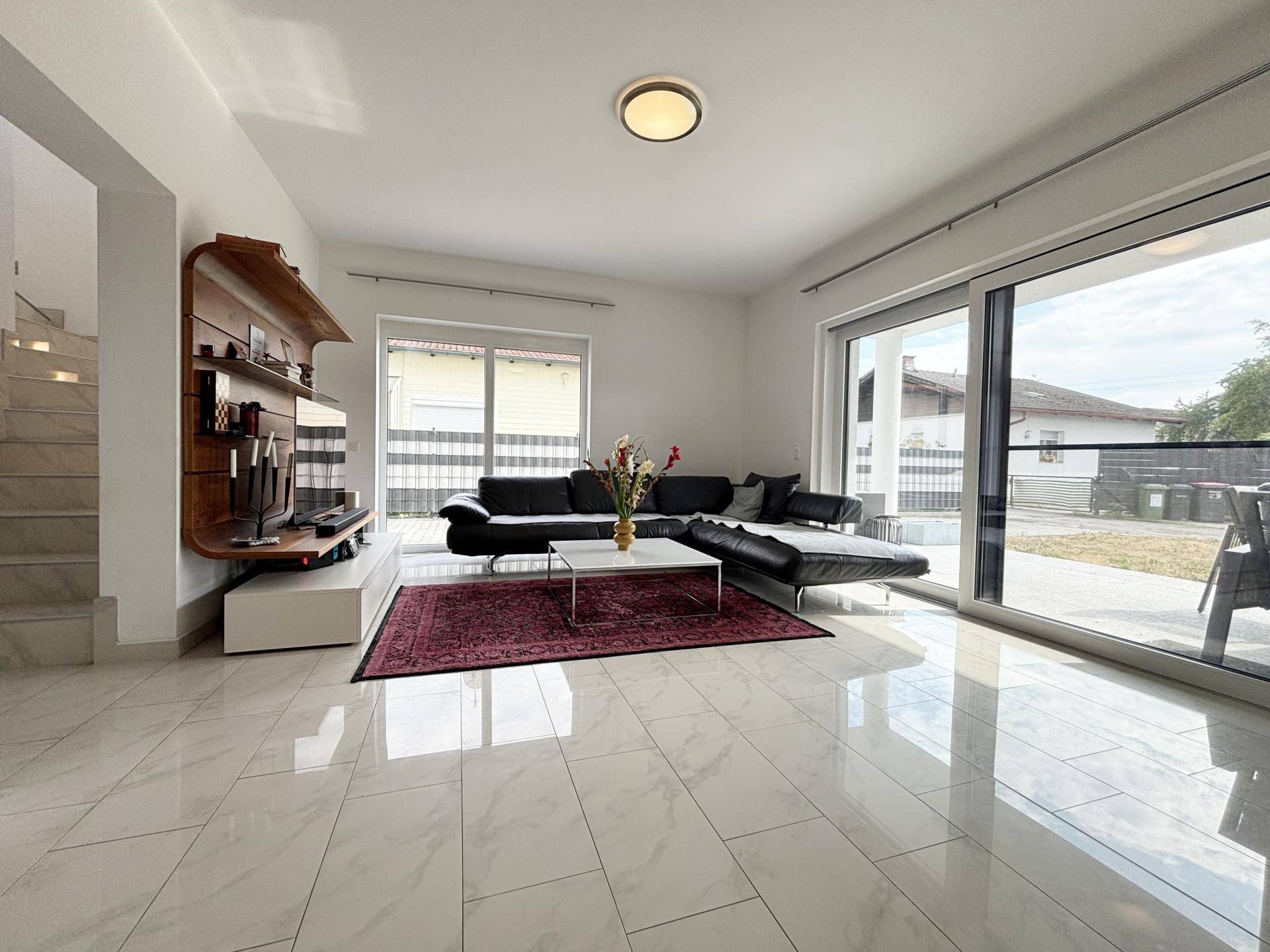 Geräumiges Wohnzimmer mit großem Sofa, Fliesenboden und Zugang zur Terrasse.
