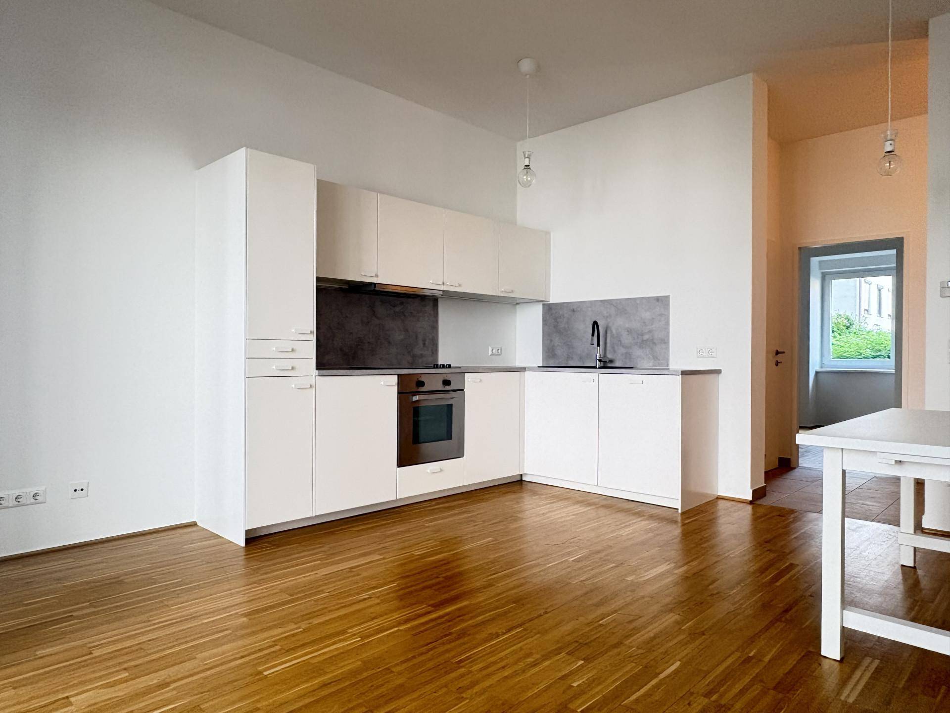 Moderne Einbauküche mit weißen Schränken, integriertem Backofen und hellem Holzfußboden.