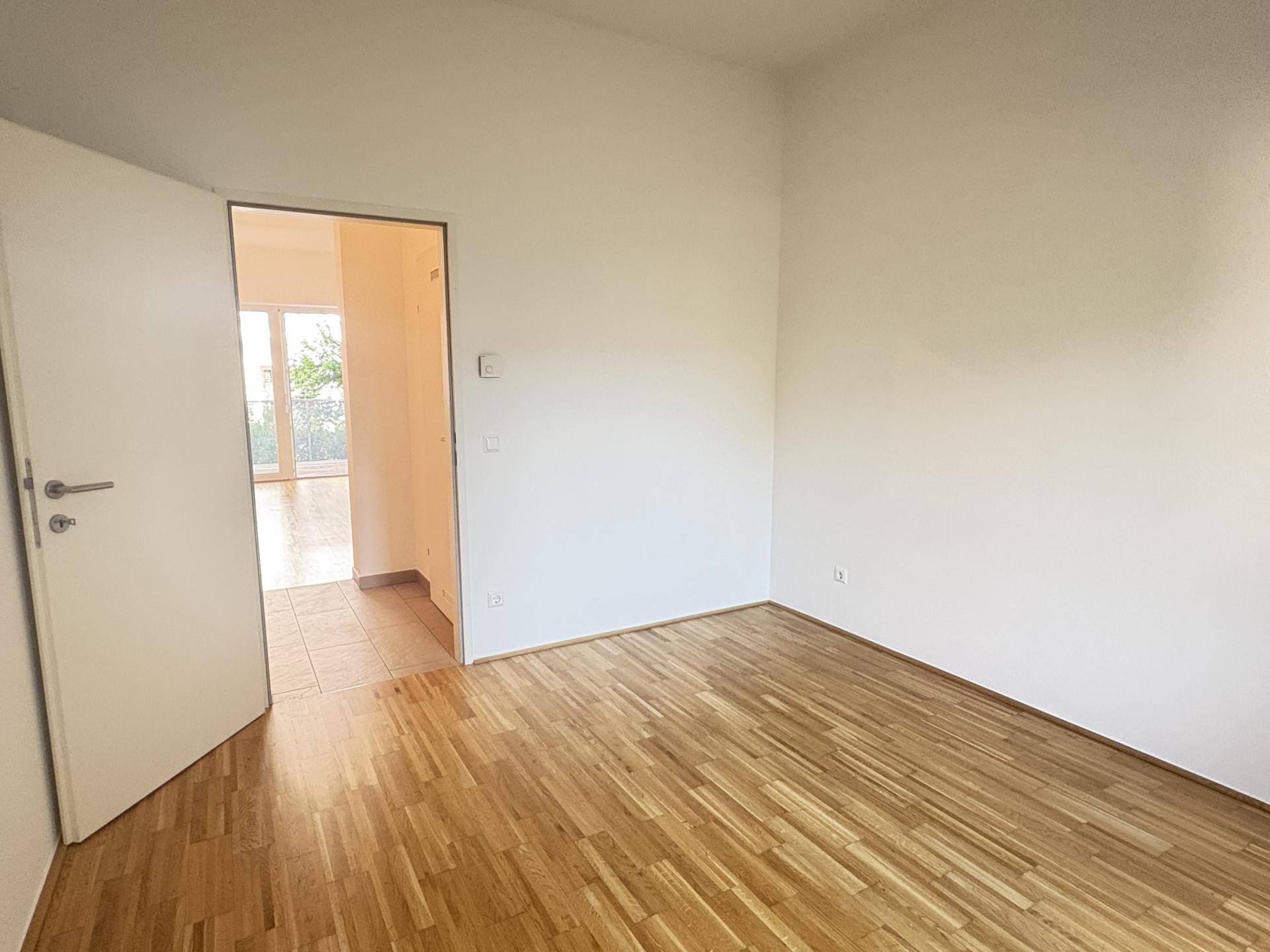 Leeres Zimmer mit hellem Holzfußboden und weiß gestrichenen Wänden, bereit zum Einzug.