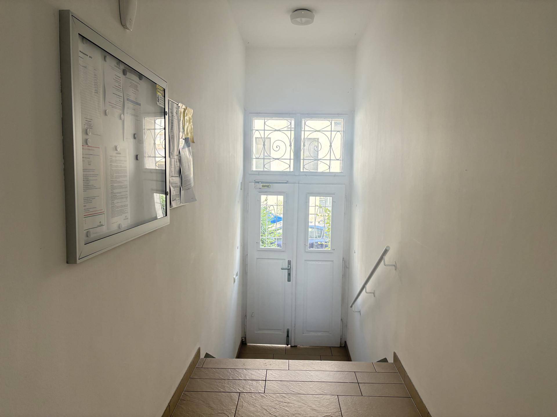 Treppenhaus mit Fliesenstufen und einer verzierten Eingangstür, die ins Freie führt.