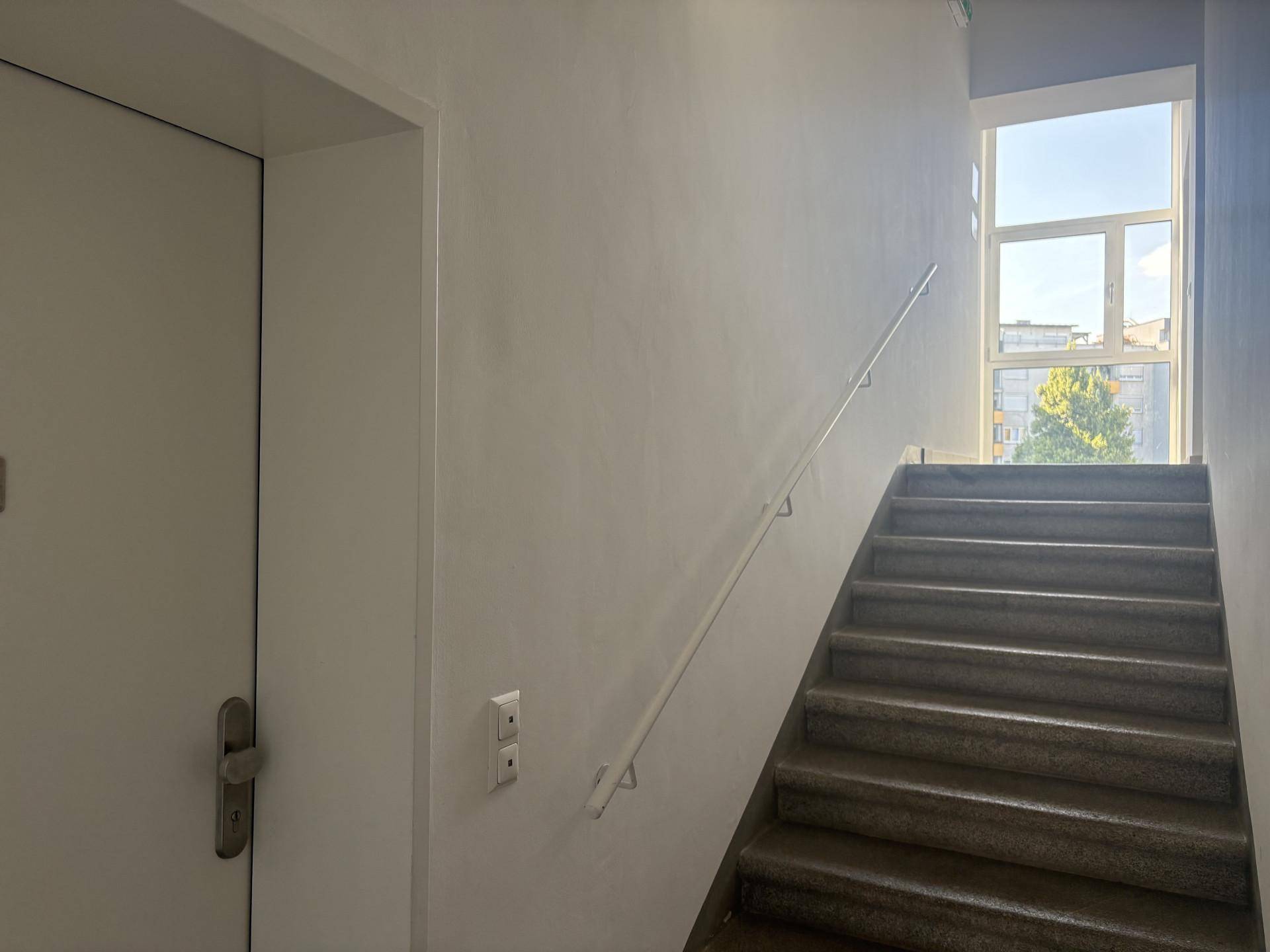 Treppenaufgang mit Handlauf und großem Fenster, das viel Tageslicht hereinlässt.