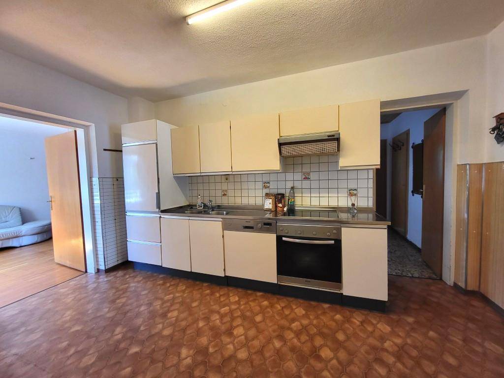 Einfache Einbauküche mit beigen Schränken, Herd und Kühlschrank, angrenzend an weitere Räume.