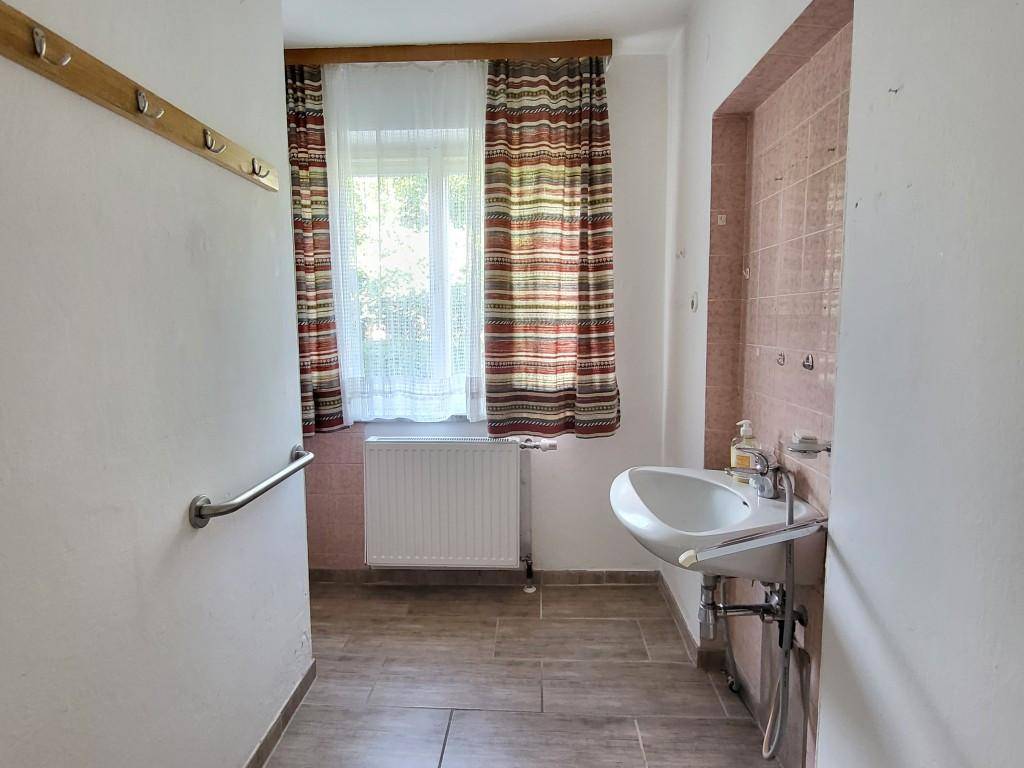 Einfaches Gäste-WC mit Waschbecken, Fenster und Haltegriffen an der Wand, funktional gestaltet.