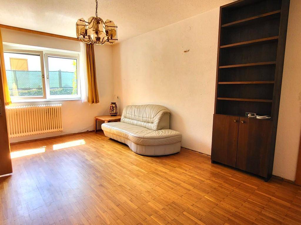 Helles Wohnzimmer mit Parkettboden, Sofa und großem Fenster, das viel Licht hereinlässt.