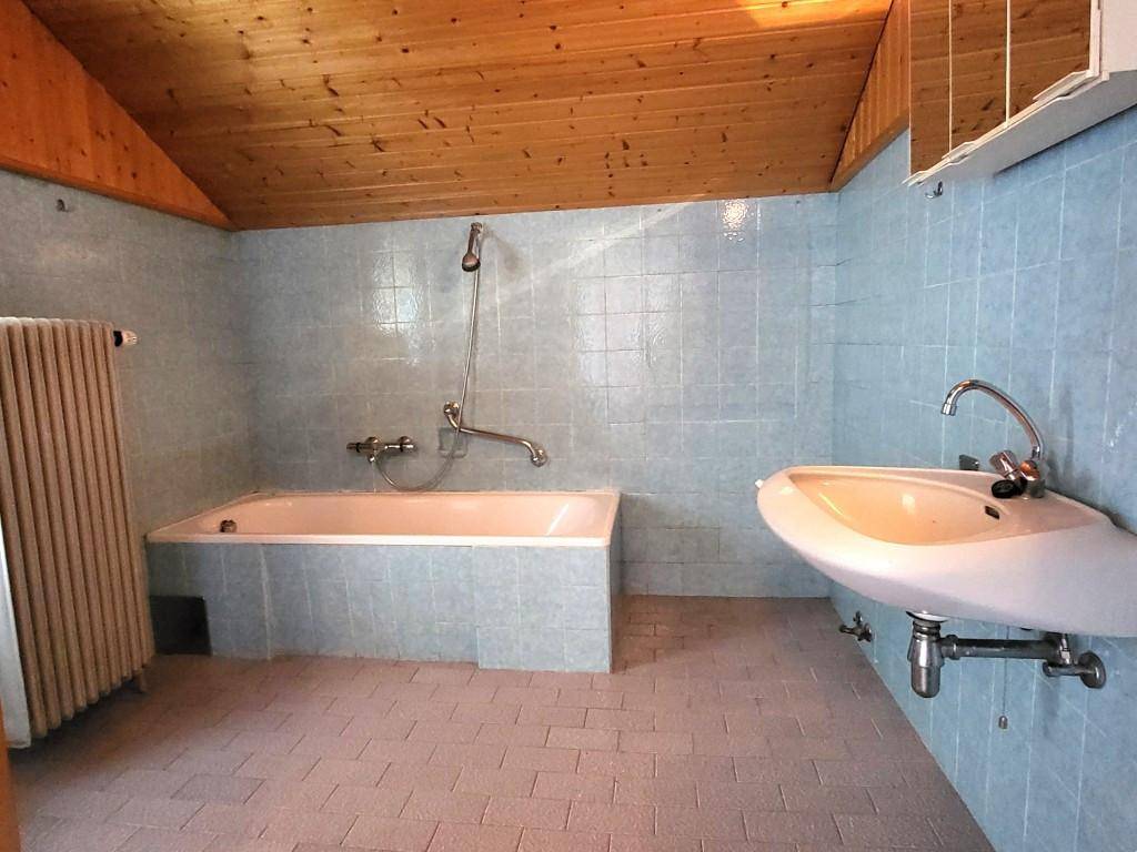 Badezimmer mit blauen Fliesen, Badewanne mit Duschfunktion und Waschbecken unter Holzdecke.