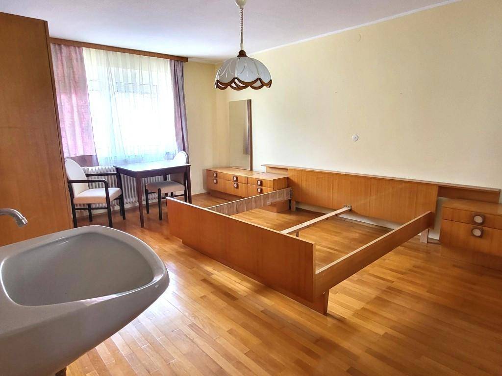 Schlafzimmer mit Holzboden, Fenster und einfacher Einrichtung, inklusive integriertem Waschbecken.