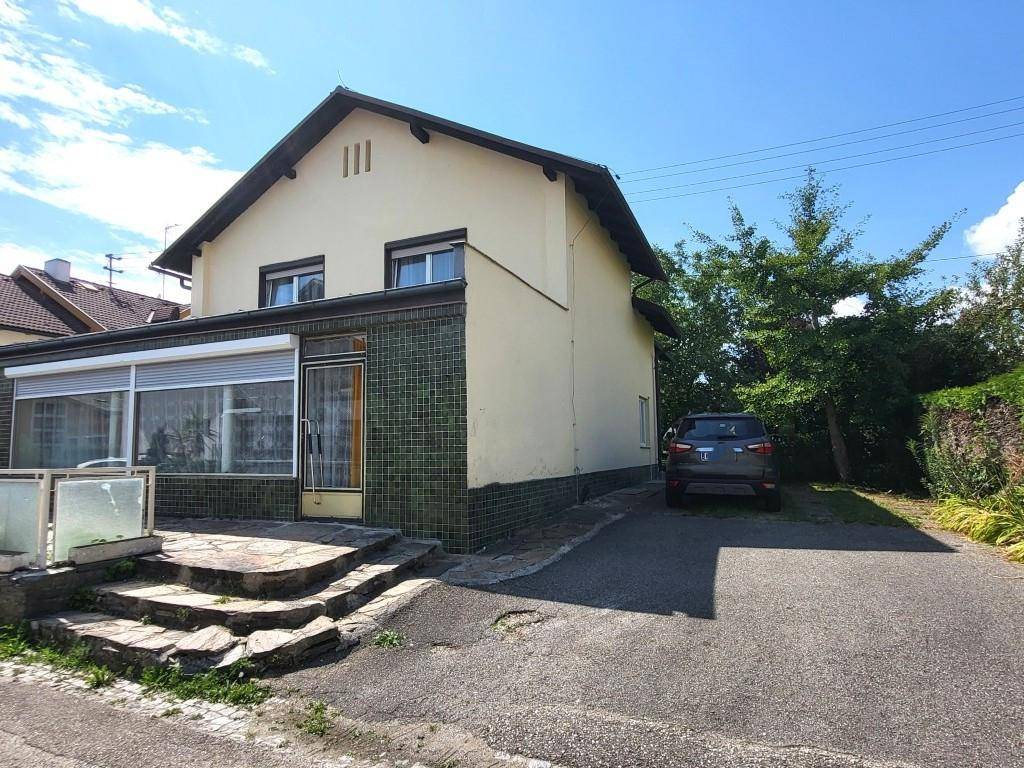Seitenansicht des Hauses mit Einfahrt, gepflasterter Fläche und sichtbaren Rollläden.