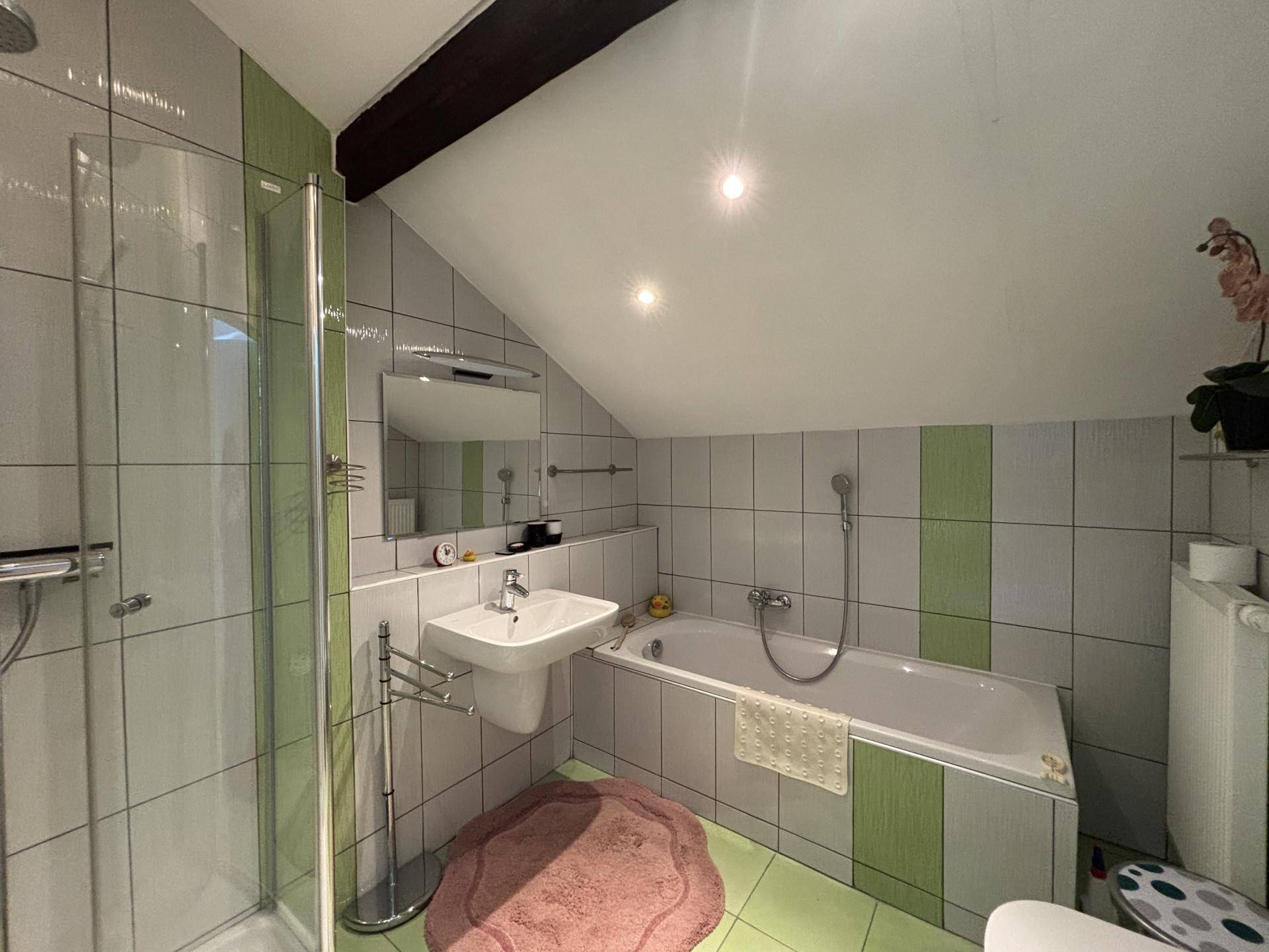 Modernes Badezimmer im Dachgeschoss mit Dusche, Badewanne und grün-weißen Fliesen.