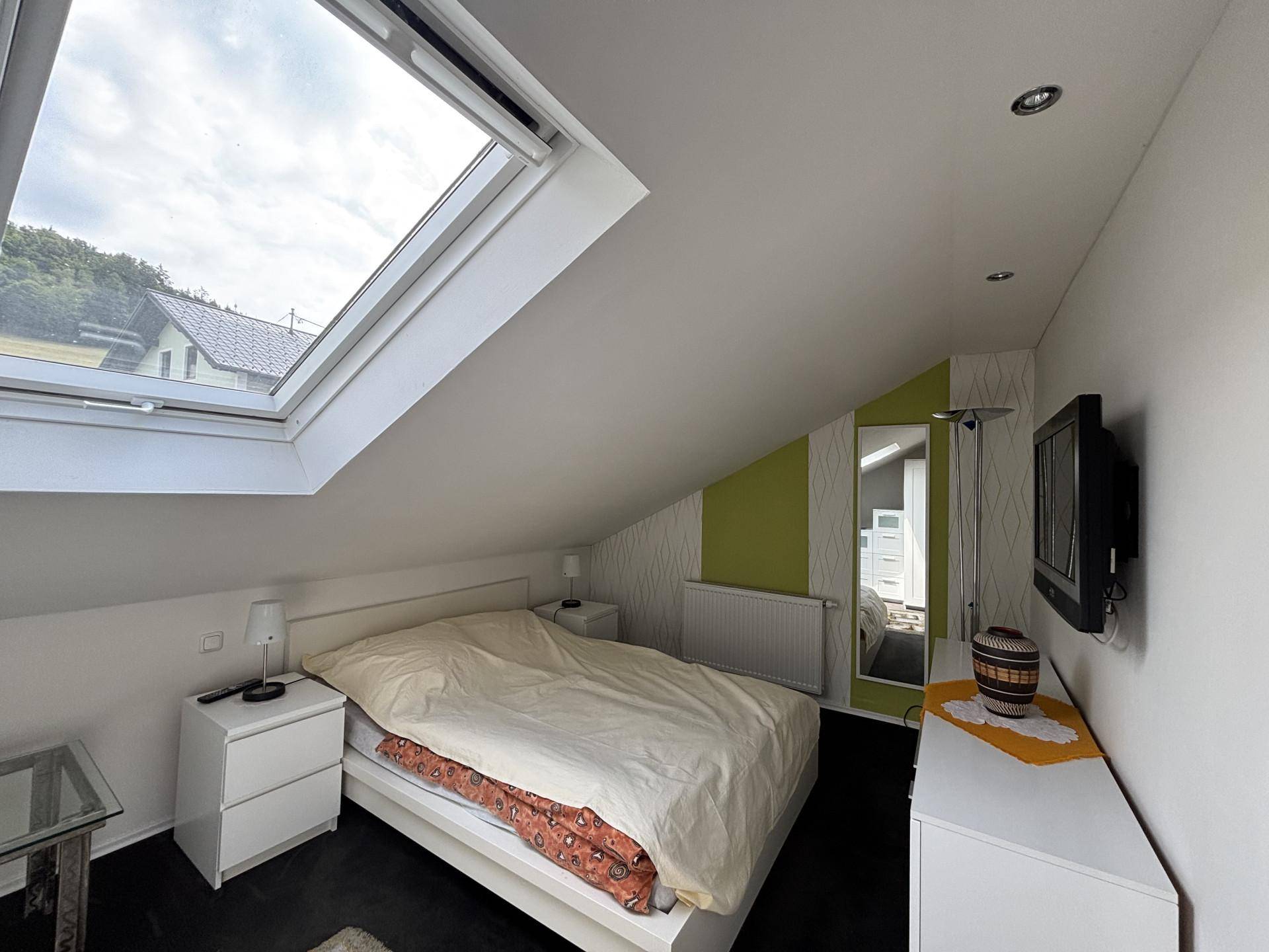 Helles Schlafzimmer im Dachgeschoss mit Dachfenster, weißem Bett und Laminatboden.